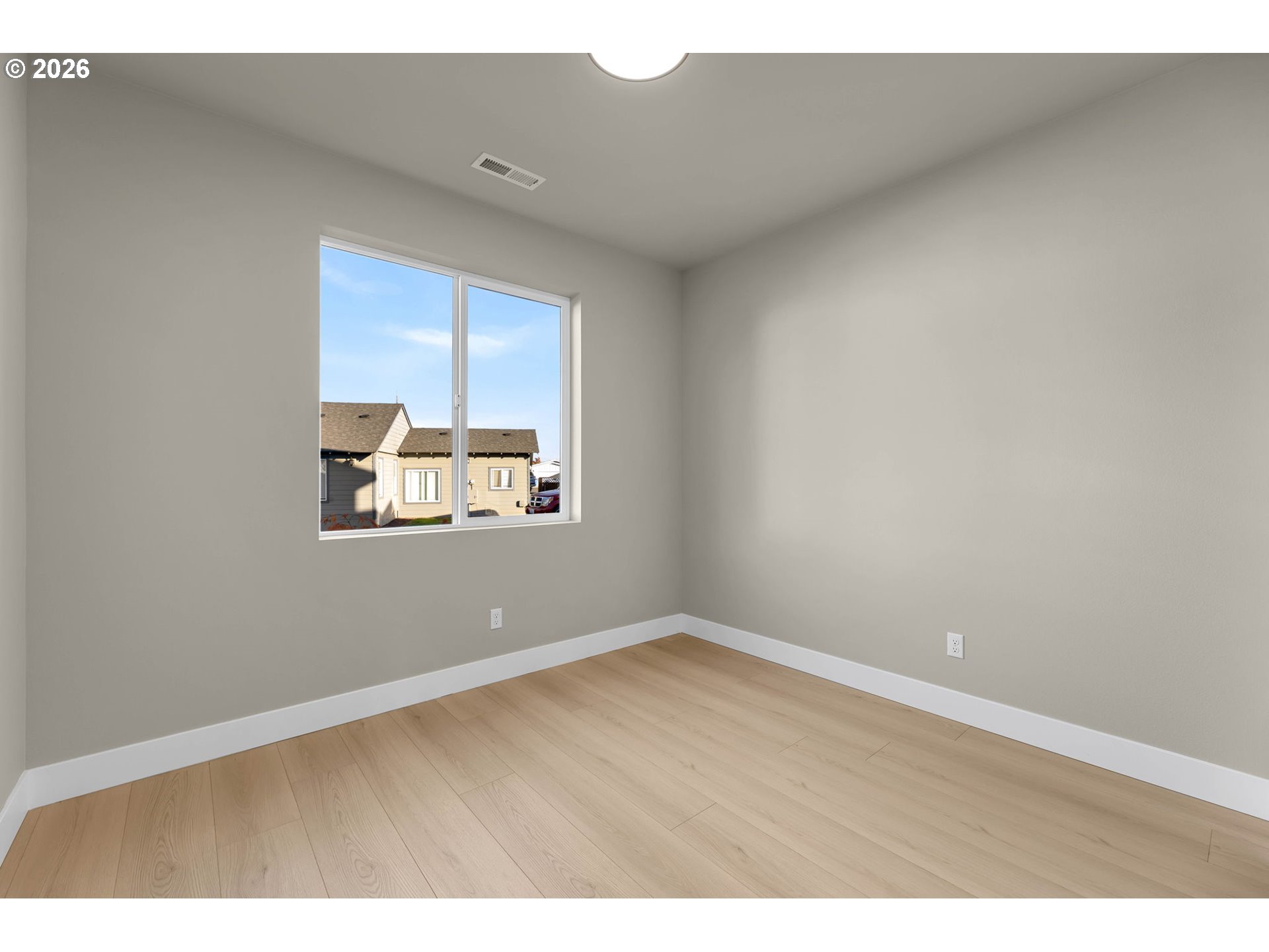 Empty room with light wood flooring and a window overlooking neighboring homes.