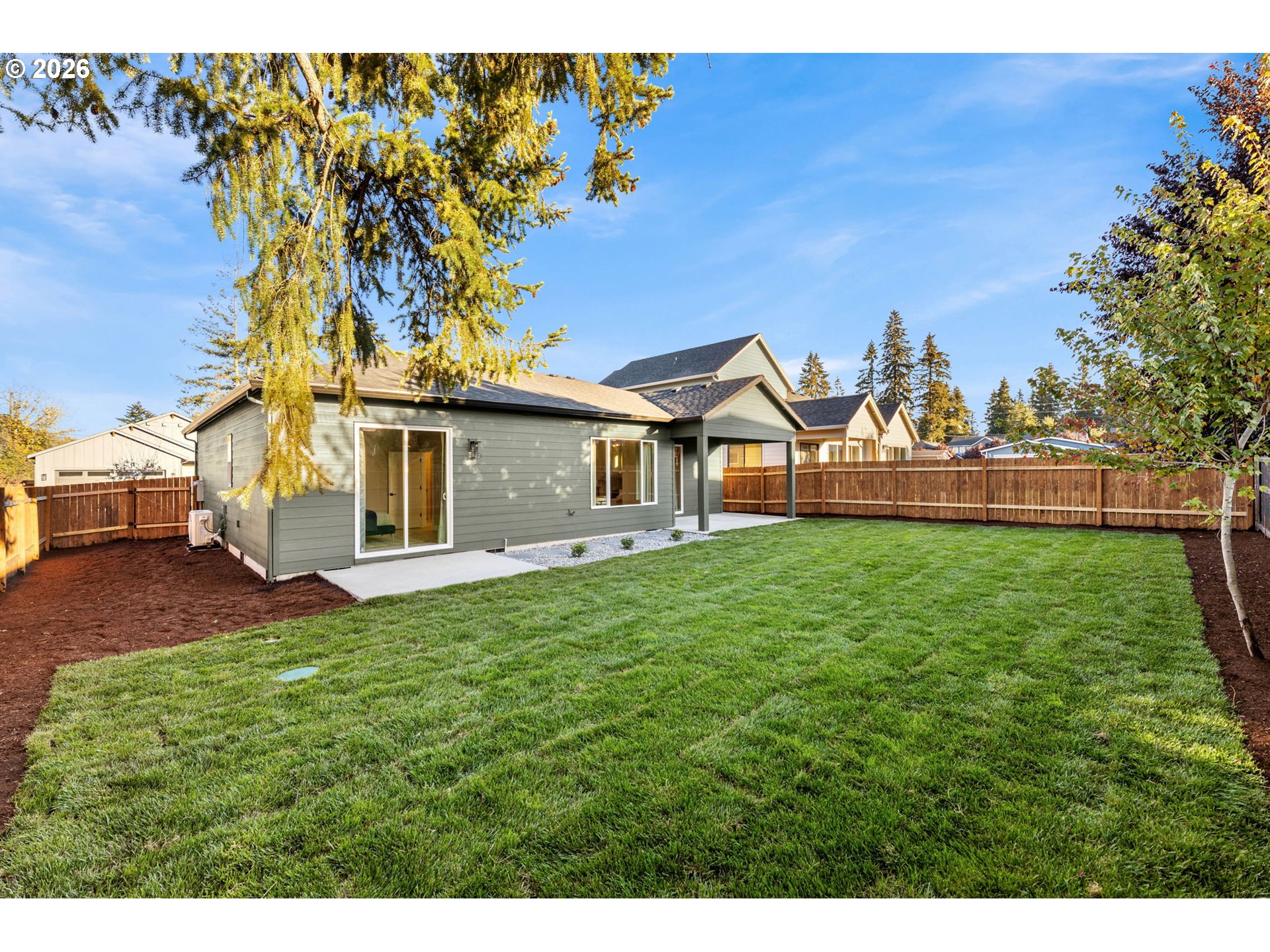 Home’s gray rear exterior and sliding door open onto a broad lawn and fenced backyard.