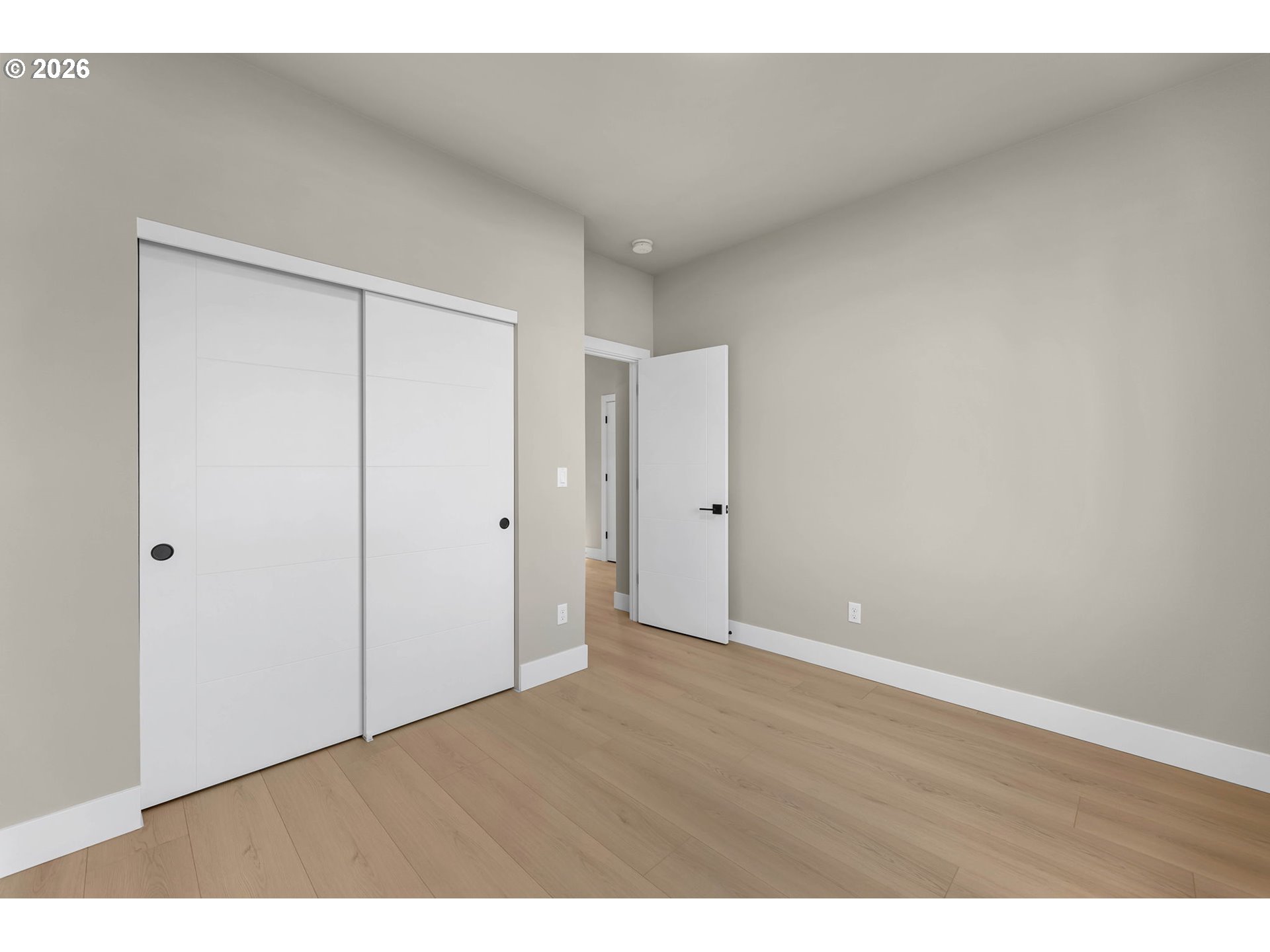 Empty bedroom with white sliding closet doors and light wood flooring.