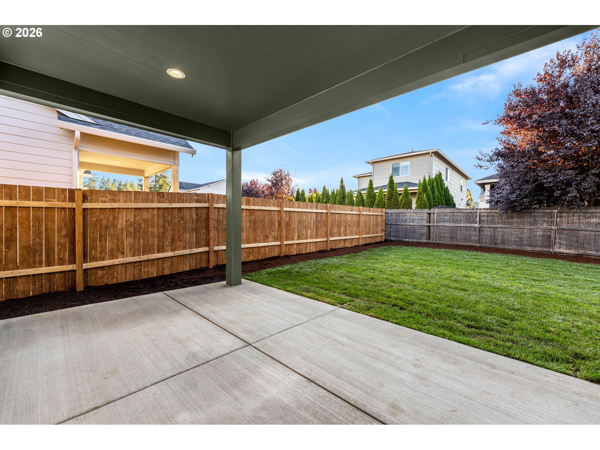 Covered patio overlooking a fenced backyard with a green lawn and mature trees.