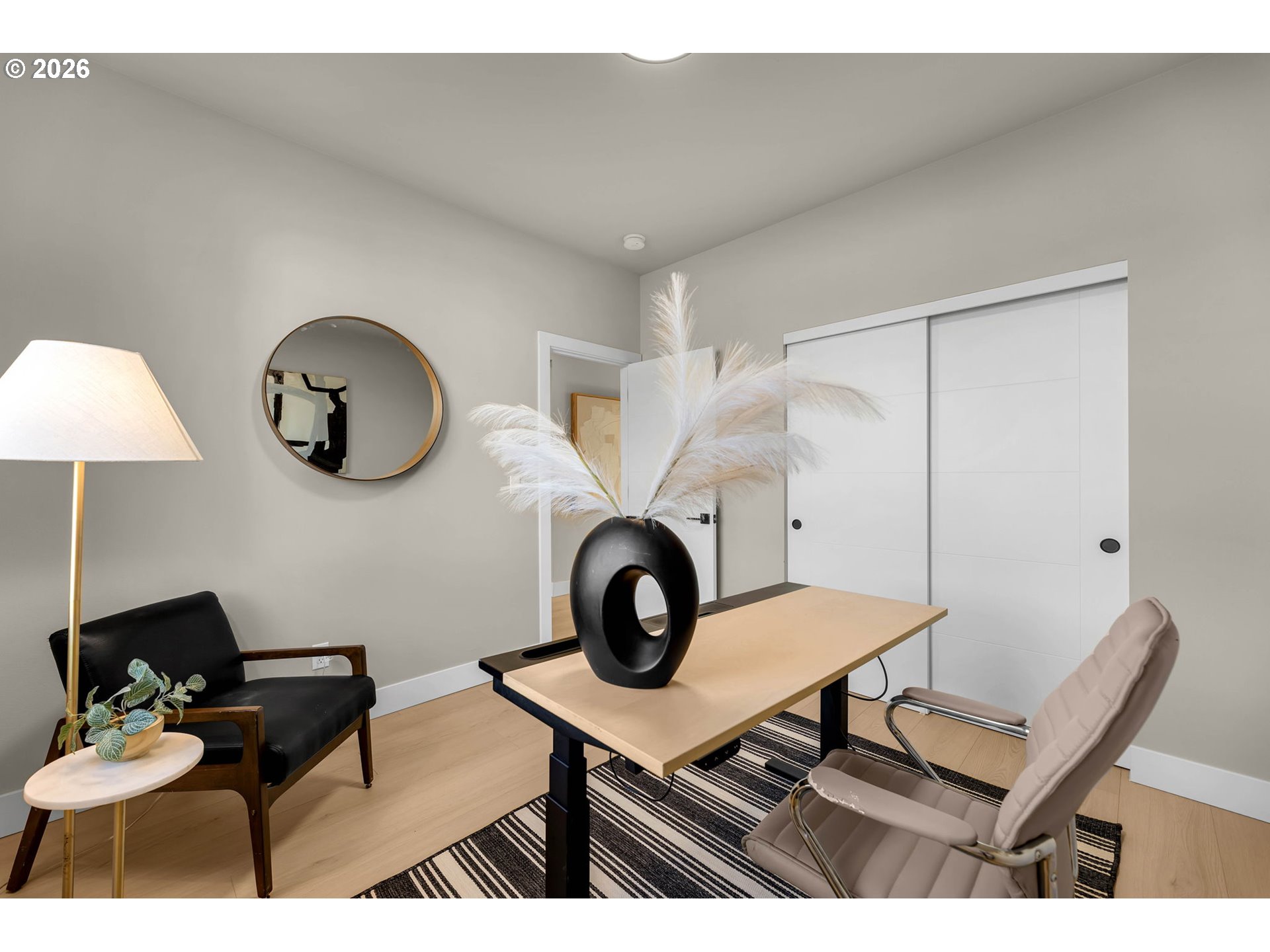 Furnished home office with a light wood desk, striped rug, and white sliding closet doors.