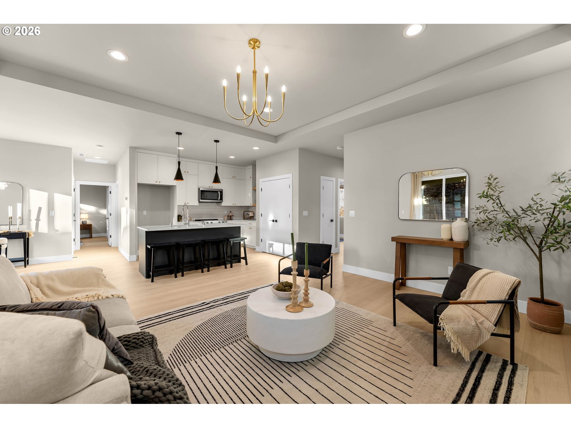 Open-plan living room and kitchen with a striped rug, black island, and brass chandelier.