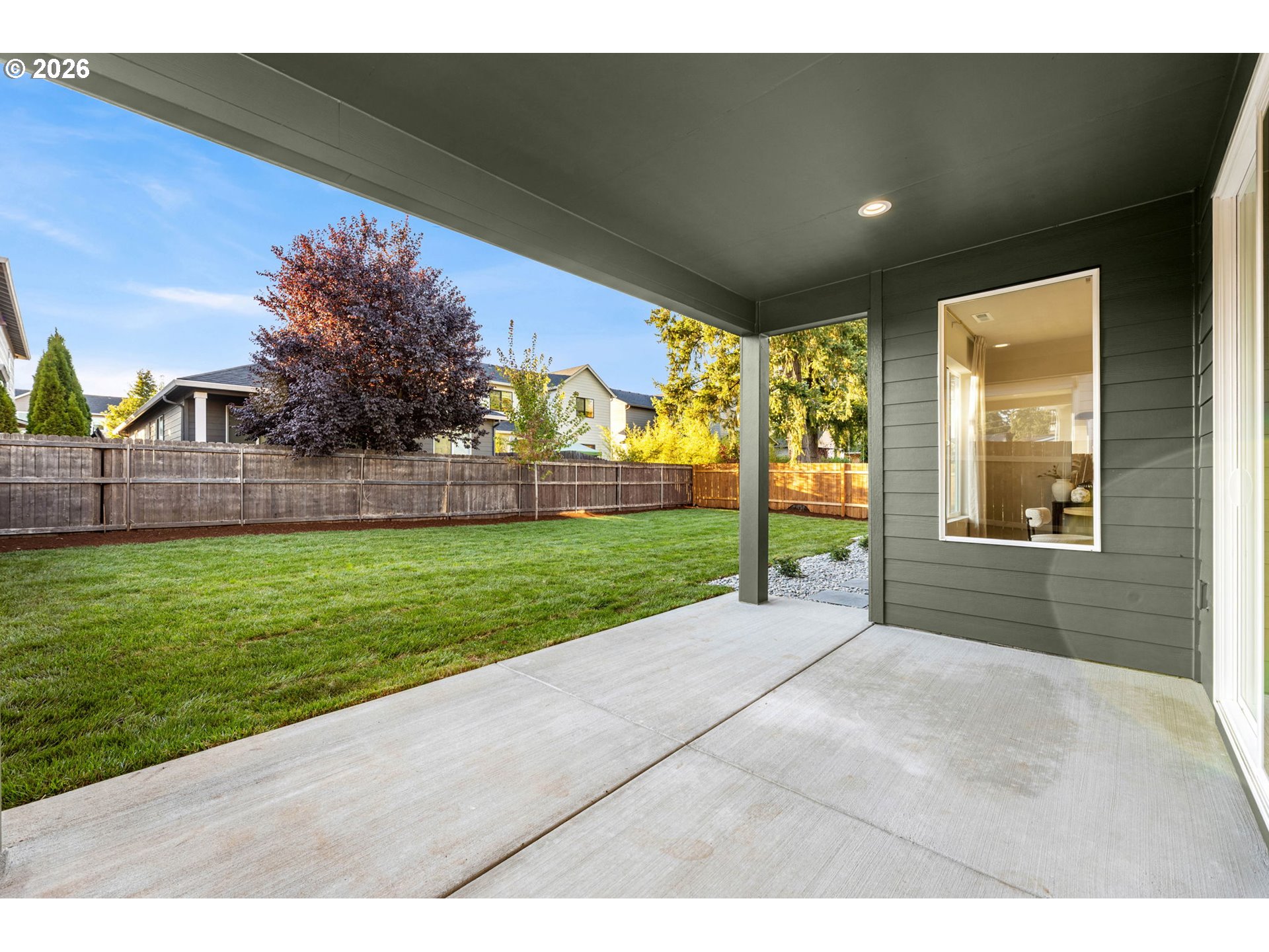 Covered patio overlooking a fenced grassy backyard with a mature tree.