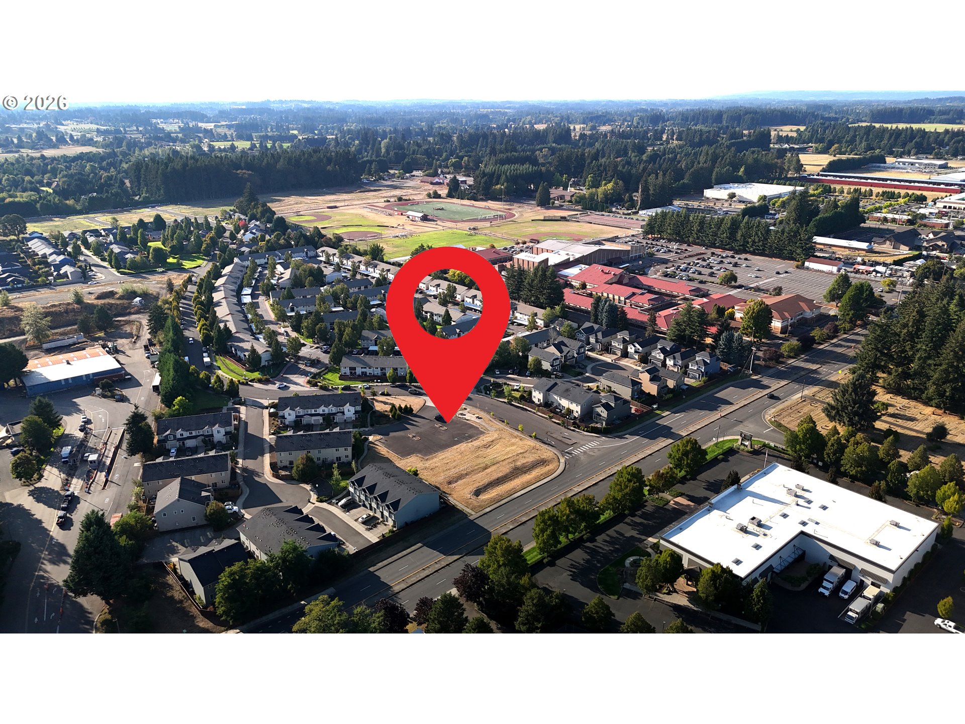Aerial neighborhood view with a red map pin marking a site beside a cleared parcel.