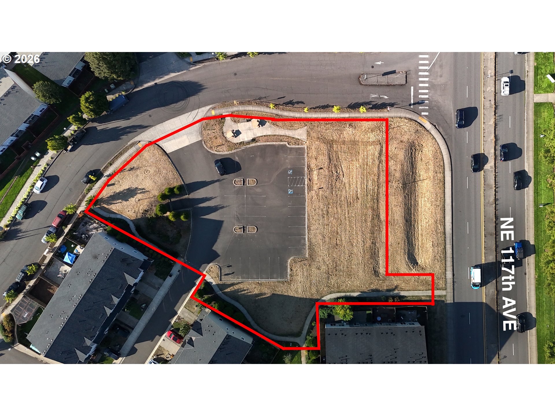 Aerial view of a vacant parcel outlined in red beside NE 117th Avenue, with a paved parking area.