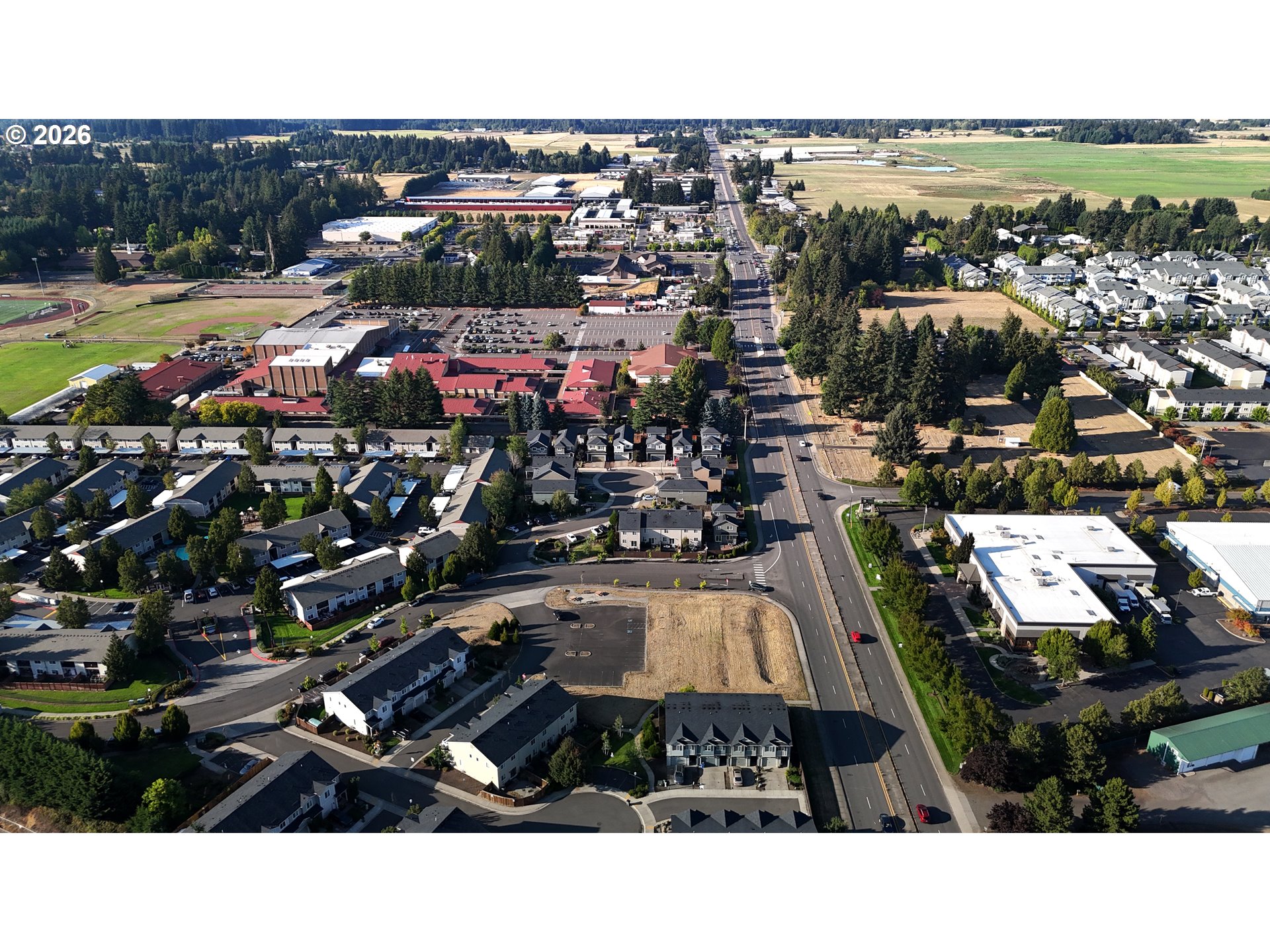 Aerial view of homes, commercial buildings, and a vacant lot beside a main road.