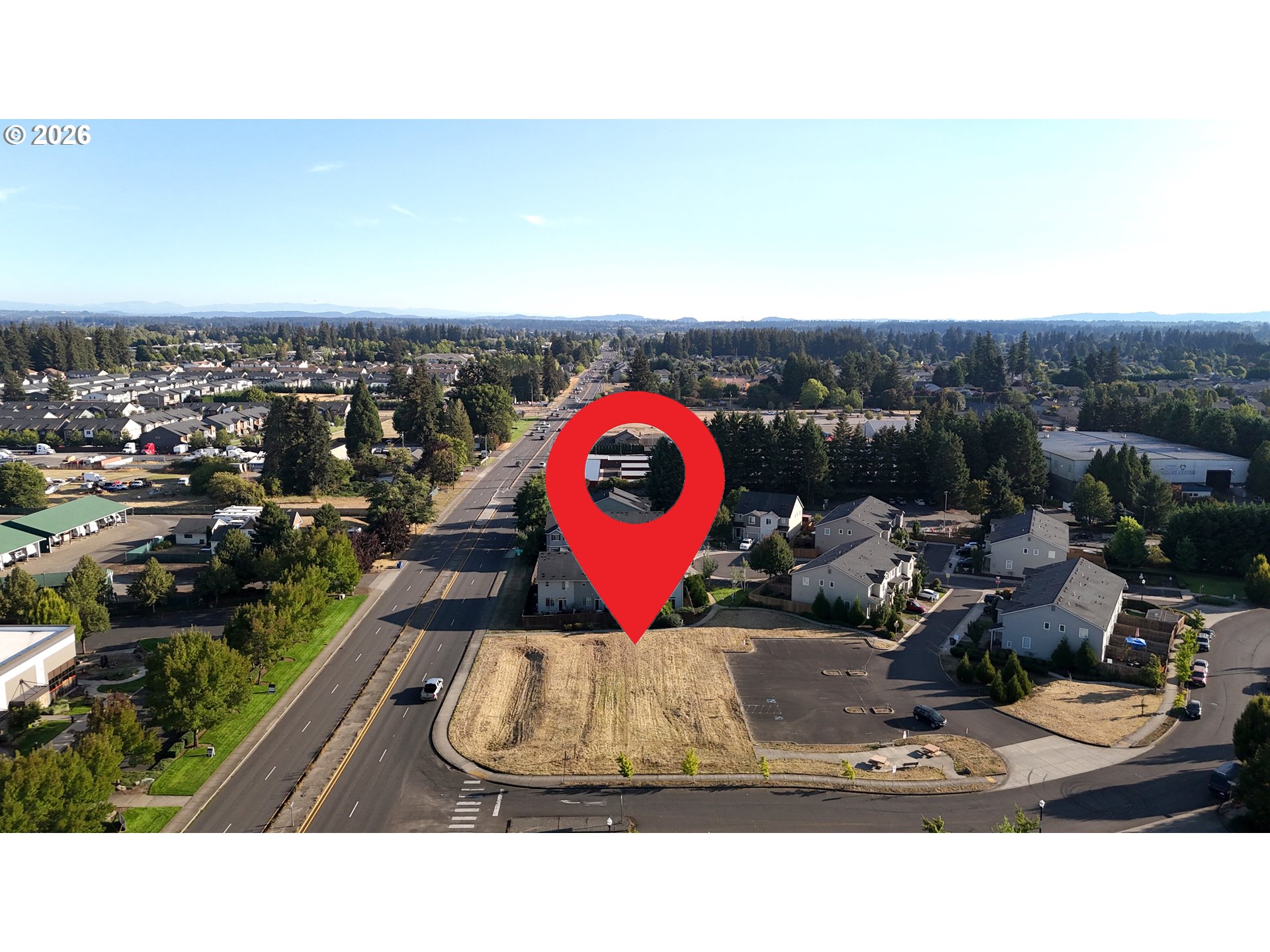 Vacant corner parcel marked by a red pin, with homes and commercial buildings nearby.