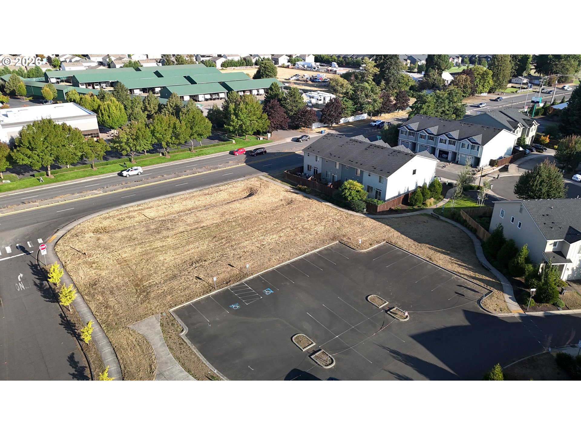 Vacant dry-grass lot beside a paved parking area, viewed from above.