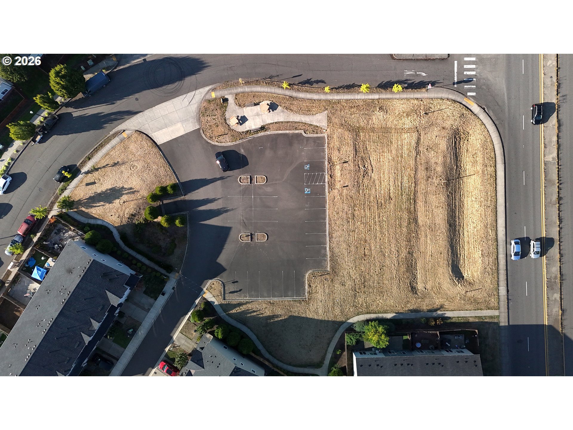 Aerial view of a dry vacant parcel beside a parking lot and roadway.
