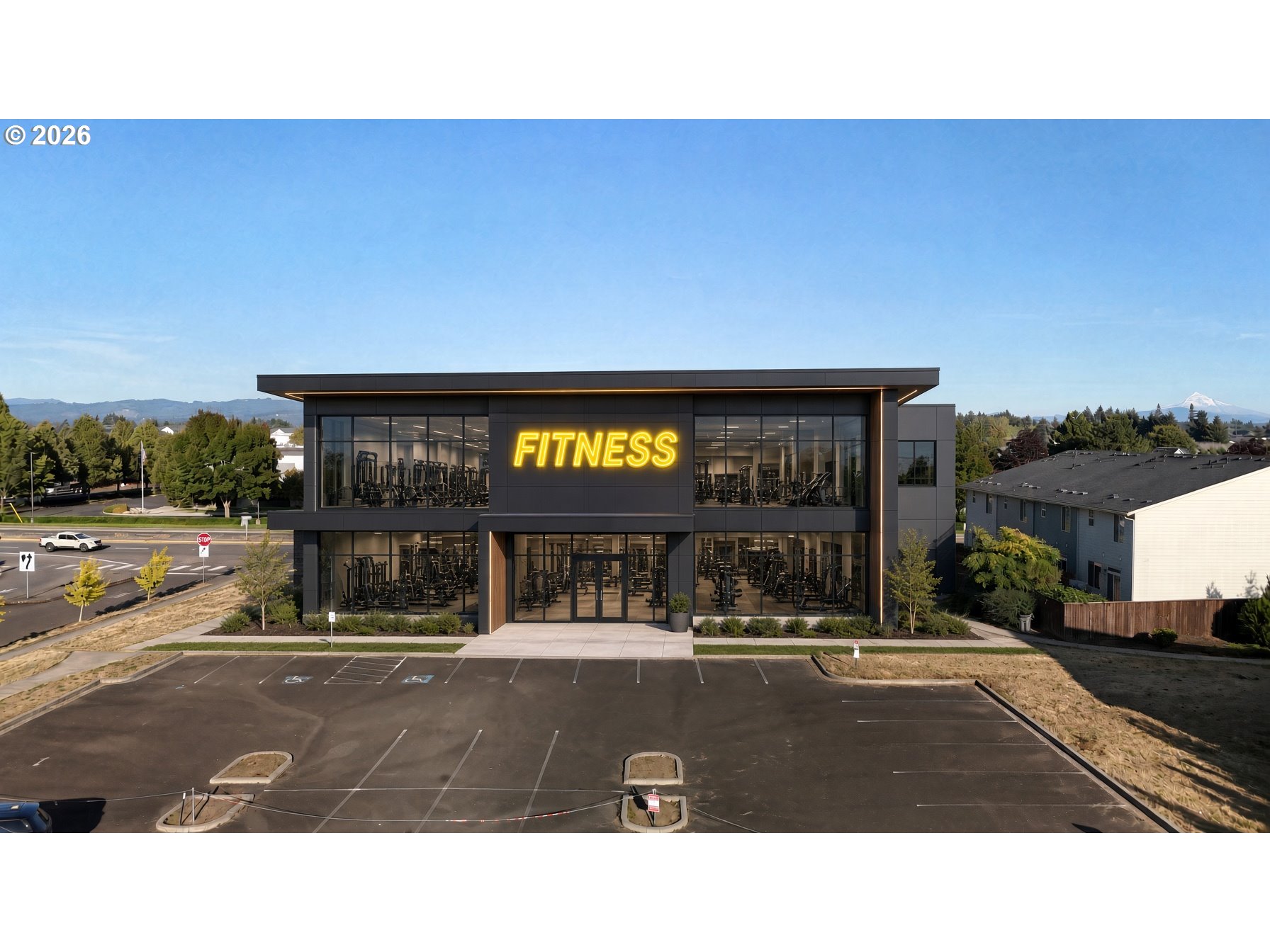 Modern fitness center with glass facade and parking lot, with a snow-capped mountain in the distance.