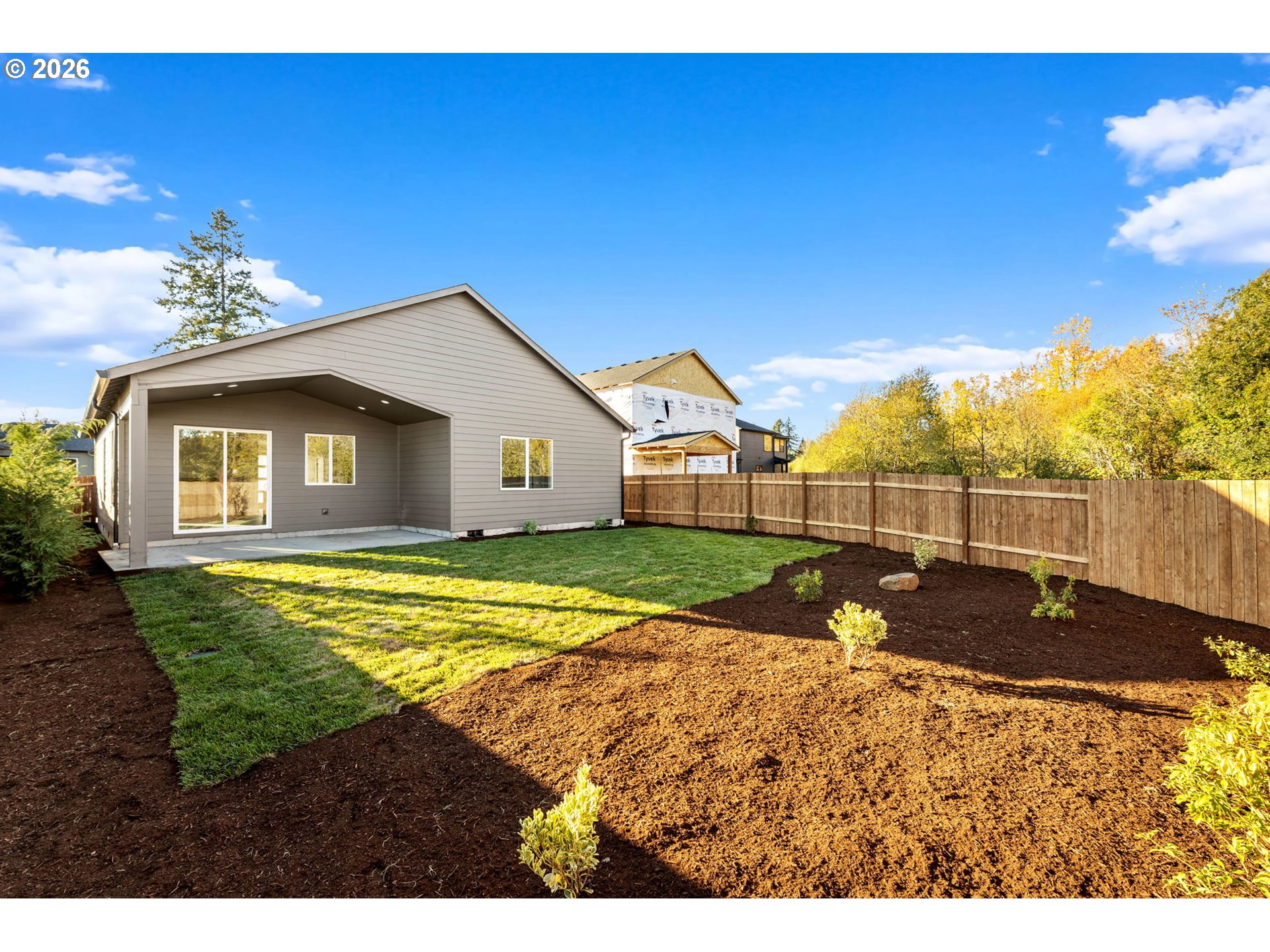Home’s rear exterior with a covered patio, fenced lawn, and landscaped mulch beds.