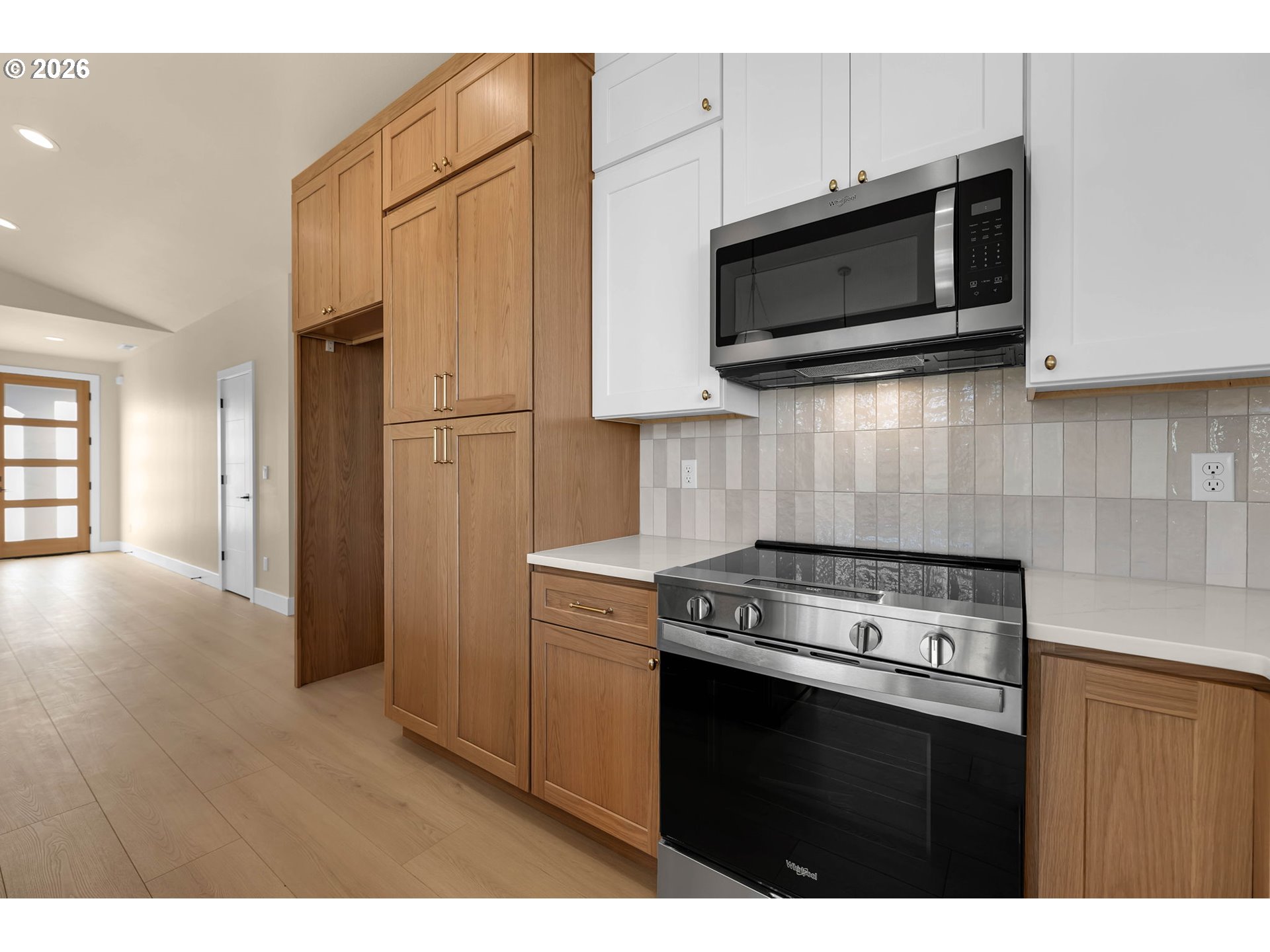 Kitchen with warm wood cabinets, white uppers, tiled backsplash, and stainless steel appliances.