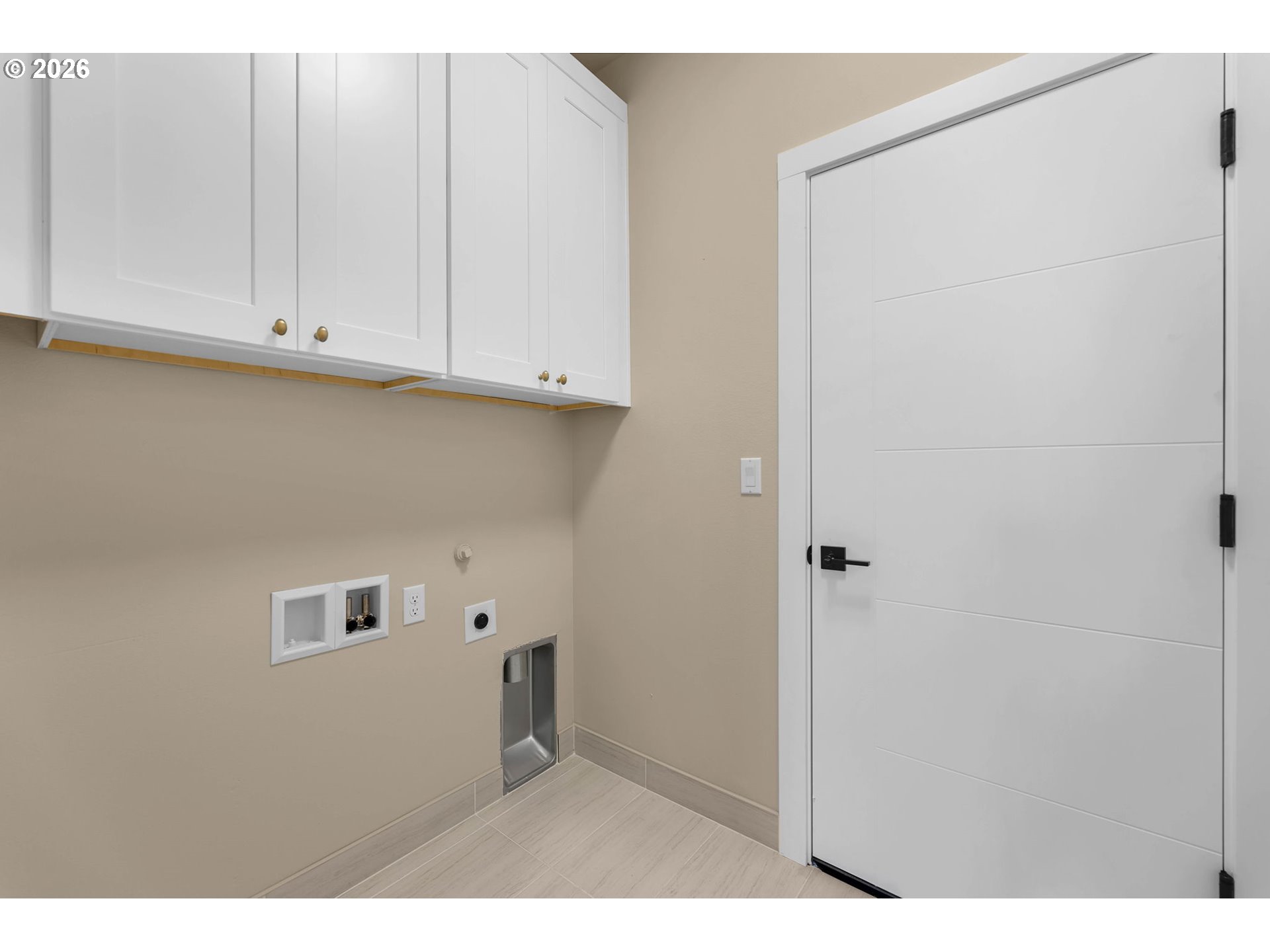 Laundry room with white upper cabinets, washer hookups, and a white door.