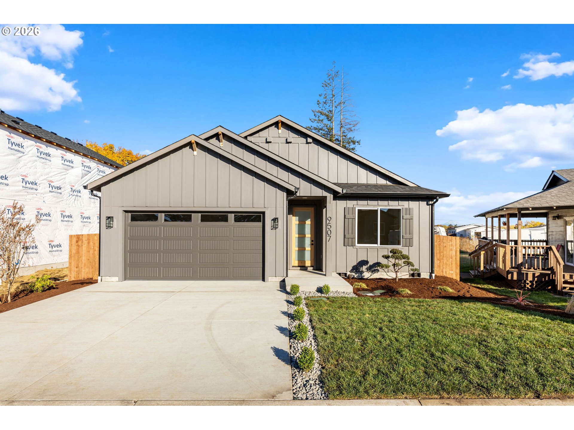 Gray gabled house with a double garage, glass-paneled entry door, and landscaped front lawn.