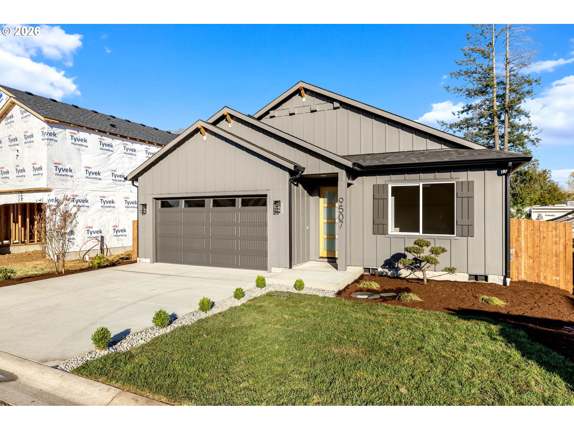 Modern gray house with a two-car garage, glass-paneled entry door, and landscaped front yard.