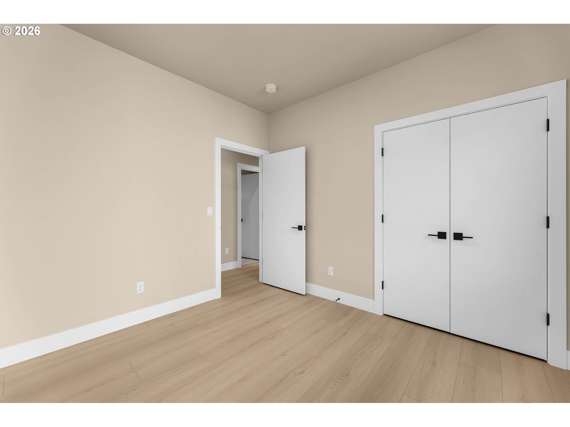Empty bedroom with light wood flooring and large white double closet doors.
