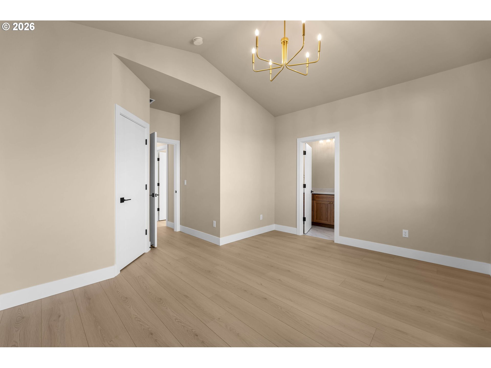 Vacant interior with light wood floors, a gold chandelier, and open doorways to adjoining rooms.