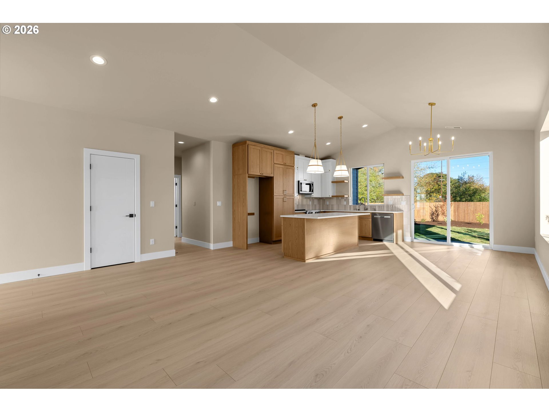 Open-plan kitchen with wood cabinetry and island, sunlight streaming through sliding glass doors to the fenced yard.