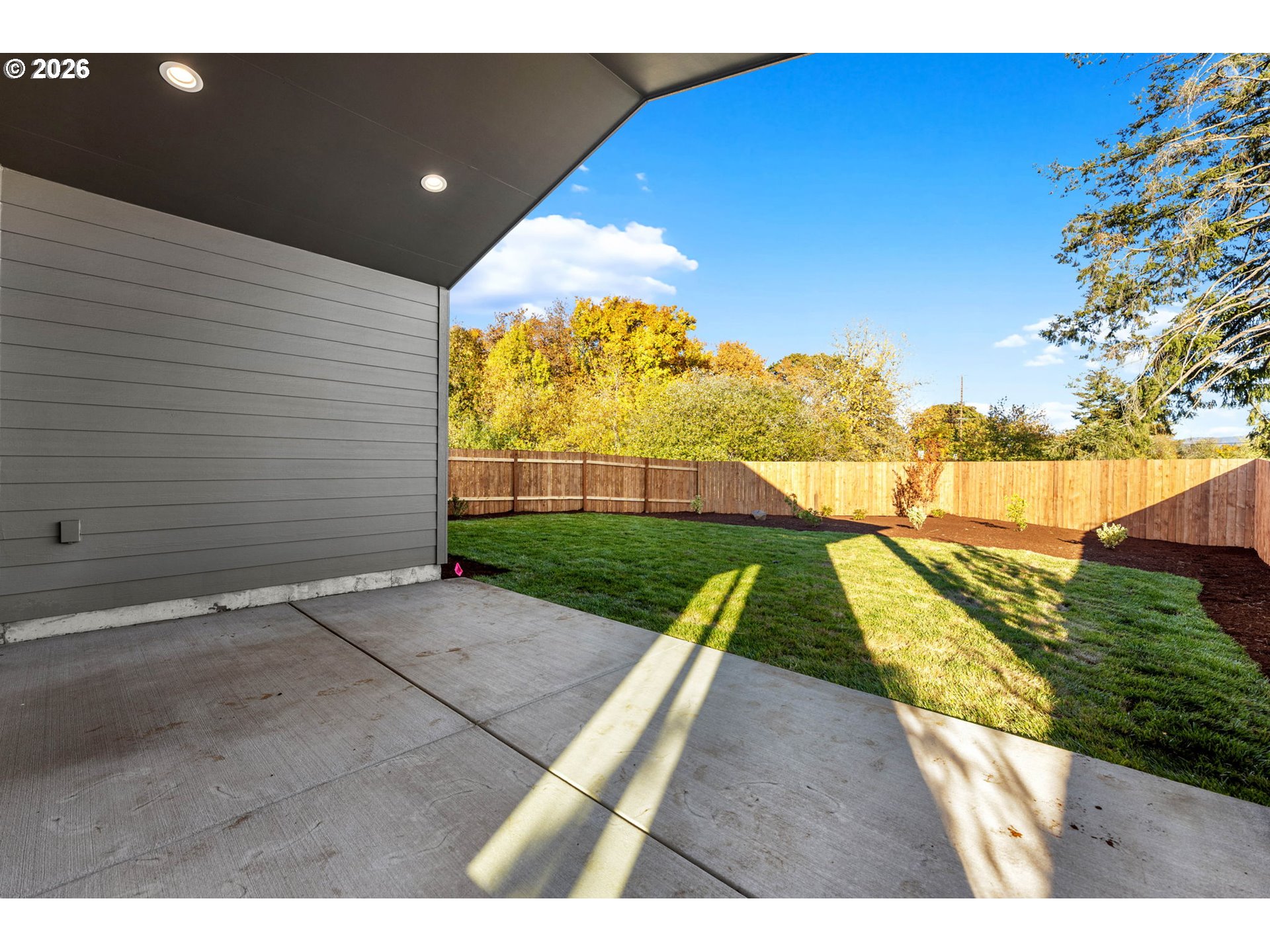 Covered concrete patio overlooking a fenced lawn and autumn trees.