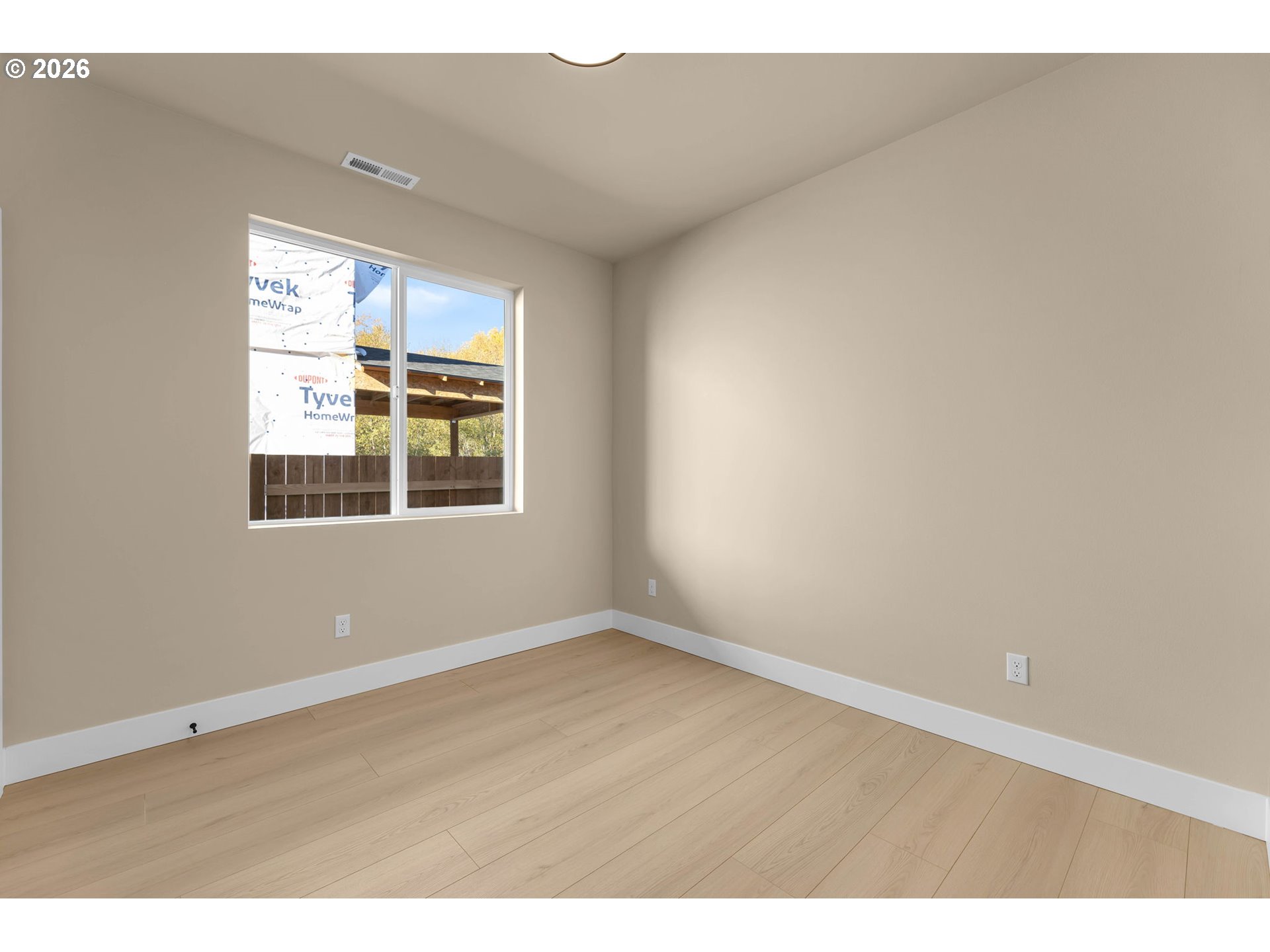 Empty room with light wood flooring and a window overlooking a fenced yard and covered patio.