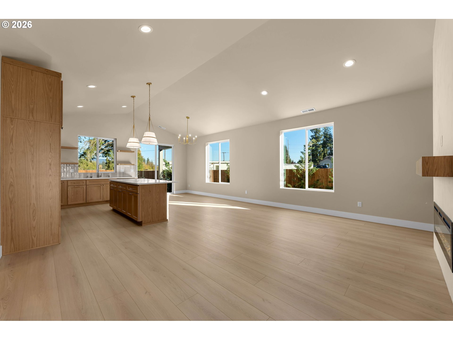 Open-plan kitchen and living area with a wood island, light plank floors, and large windows.