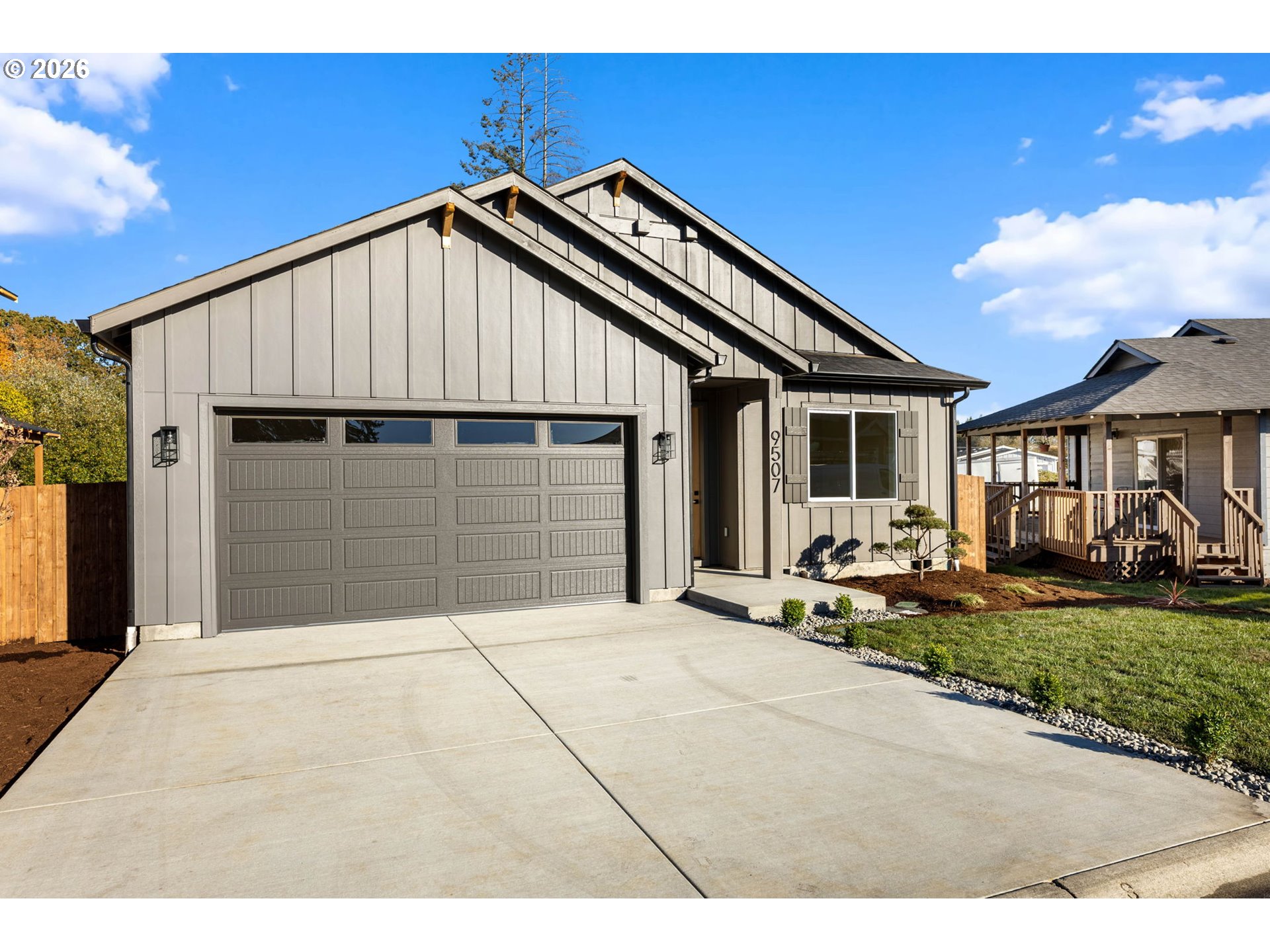Gray home with a large double garage, broad driveway, covered entry, and landscaped front yard.