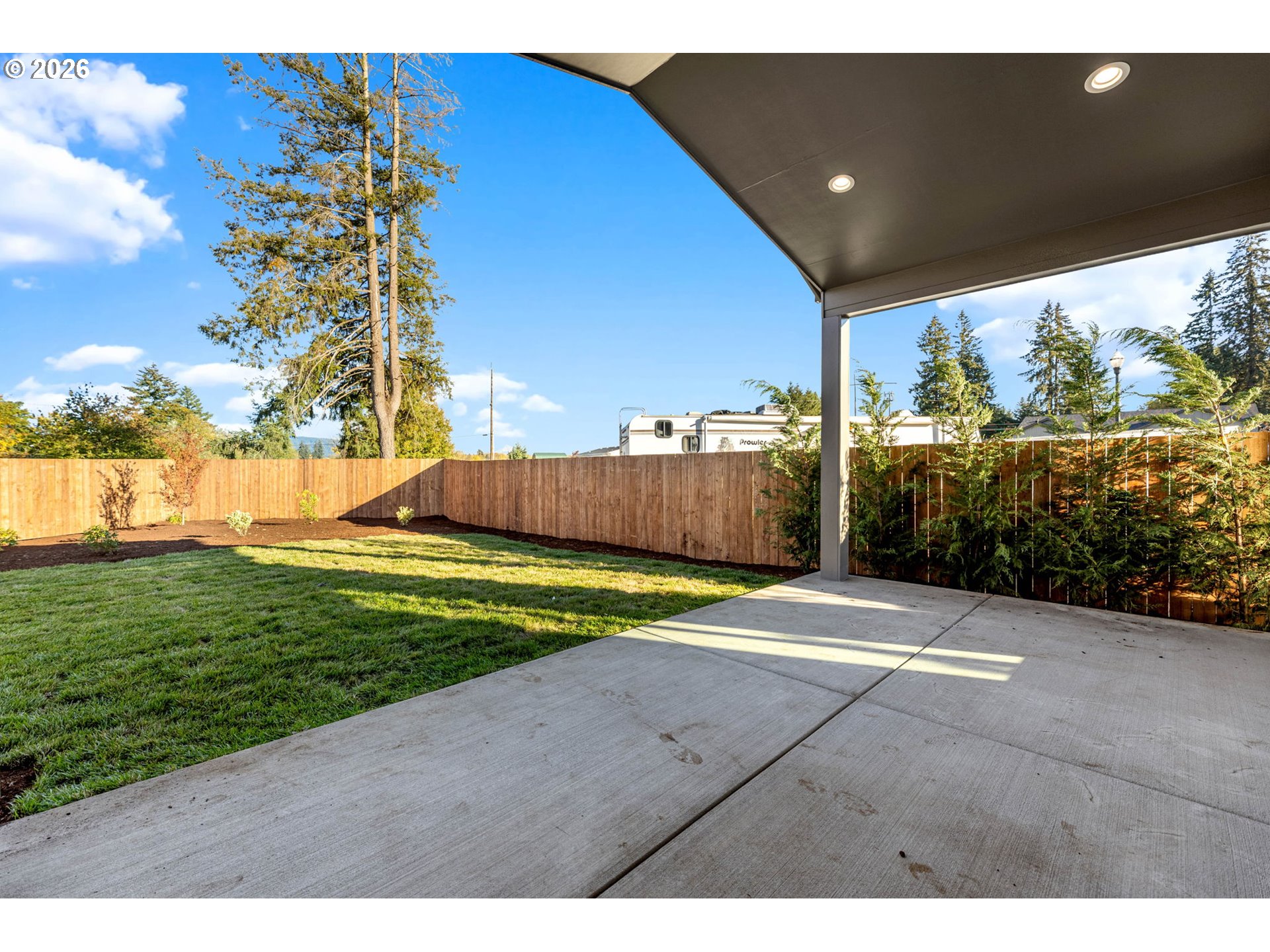 Covered concrete patio overlooking a fenced lawn and landscaped backyard.
