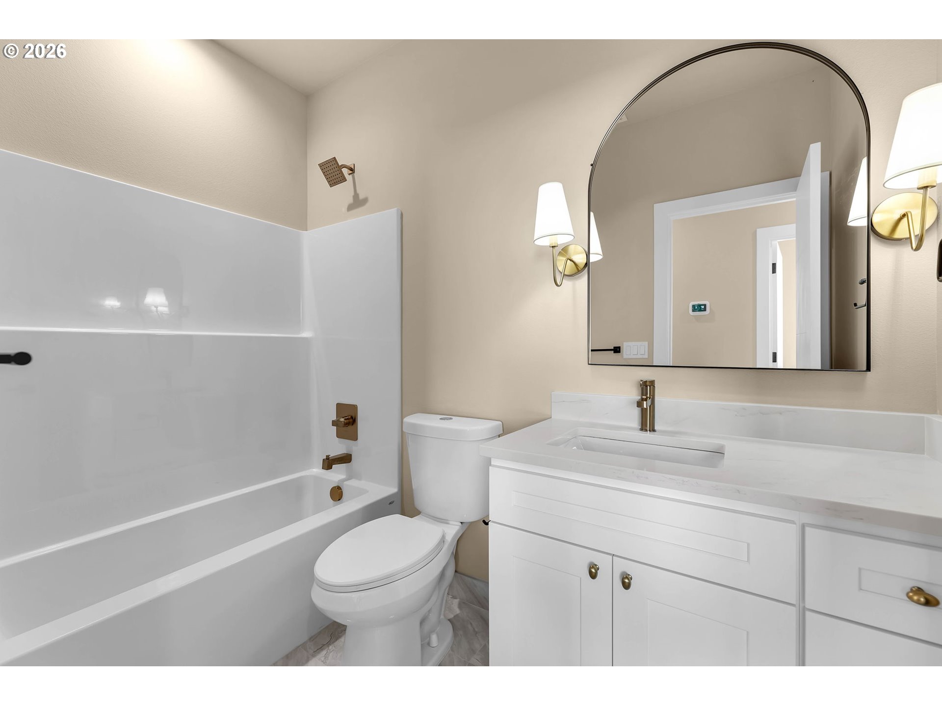 Bathroom with a white tub, toilet, and vanity beneath a large arched mirror.