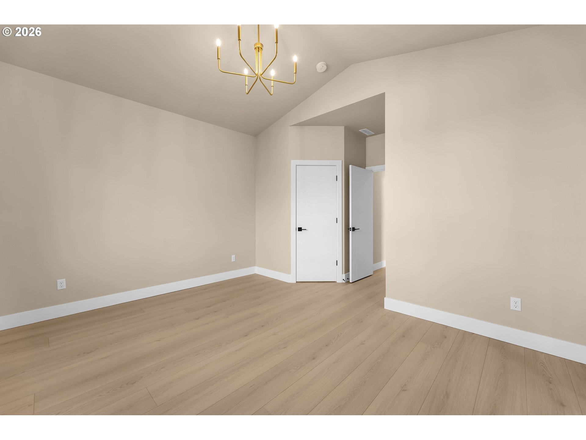 Empty dining room with light wood floors, a vaulted ceiling, and a modern gold chandelier.