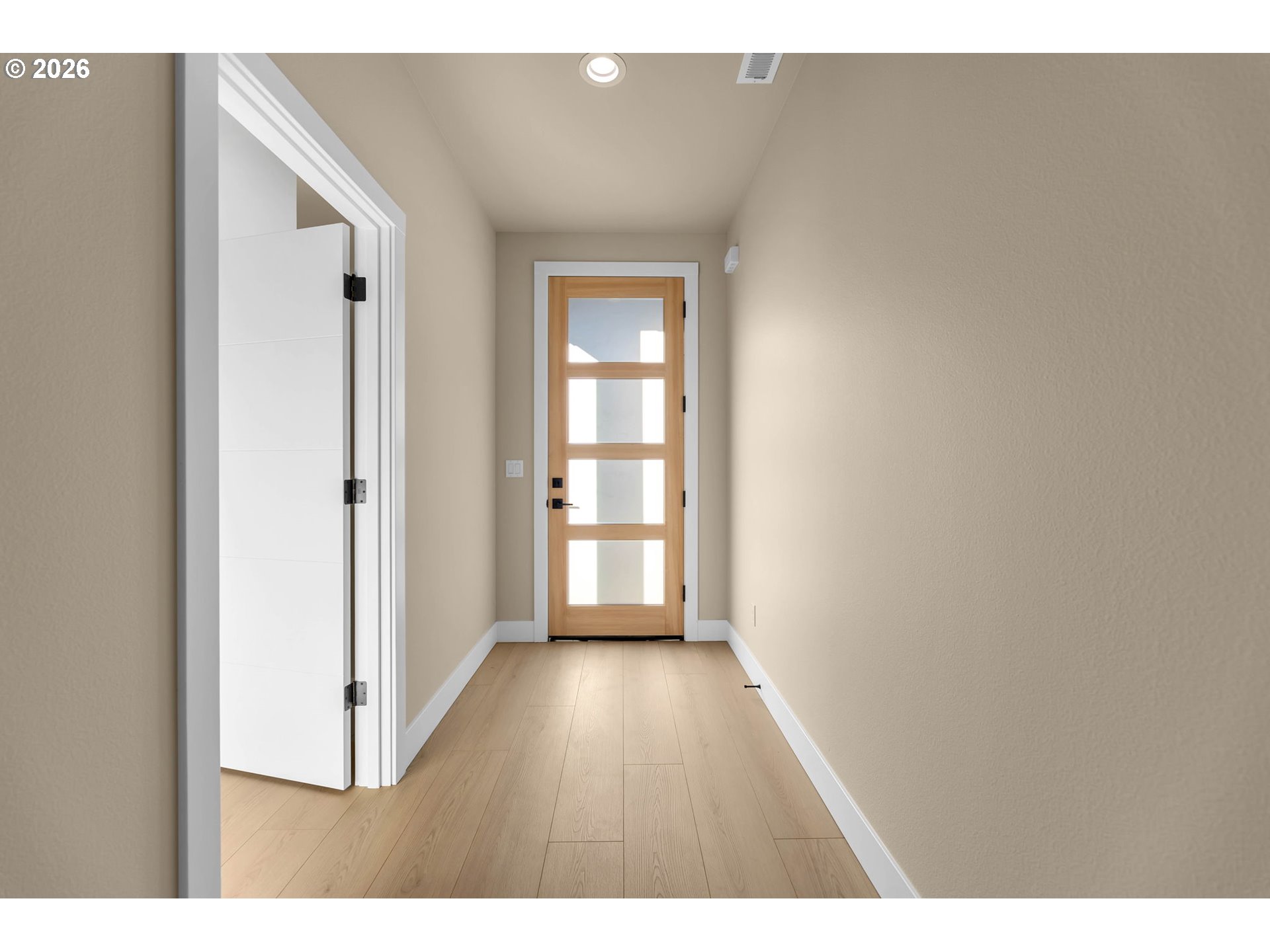 Entry hall with light wood floors and a natural wood front door with glass panels.