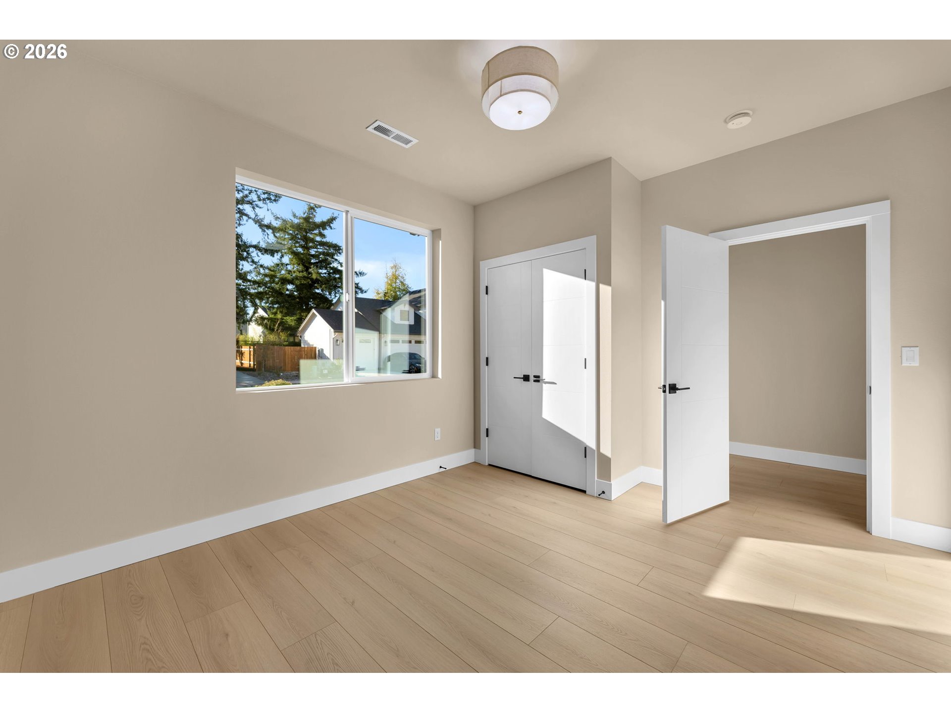 Empty room with light wood floors, white doors, and a large window.