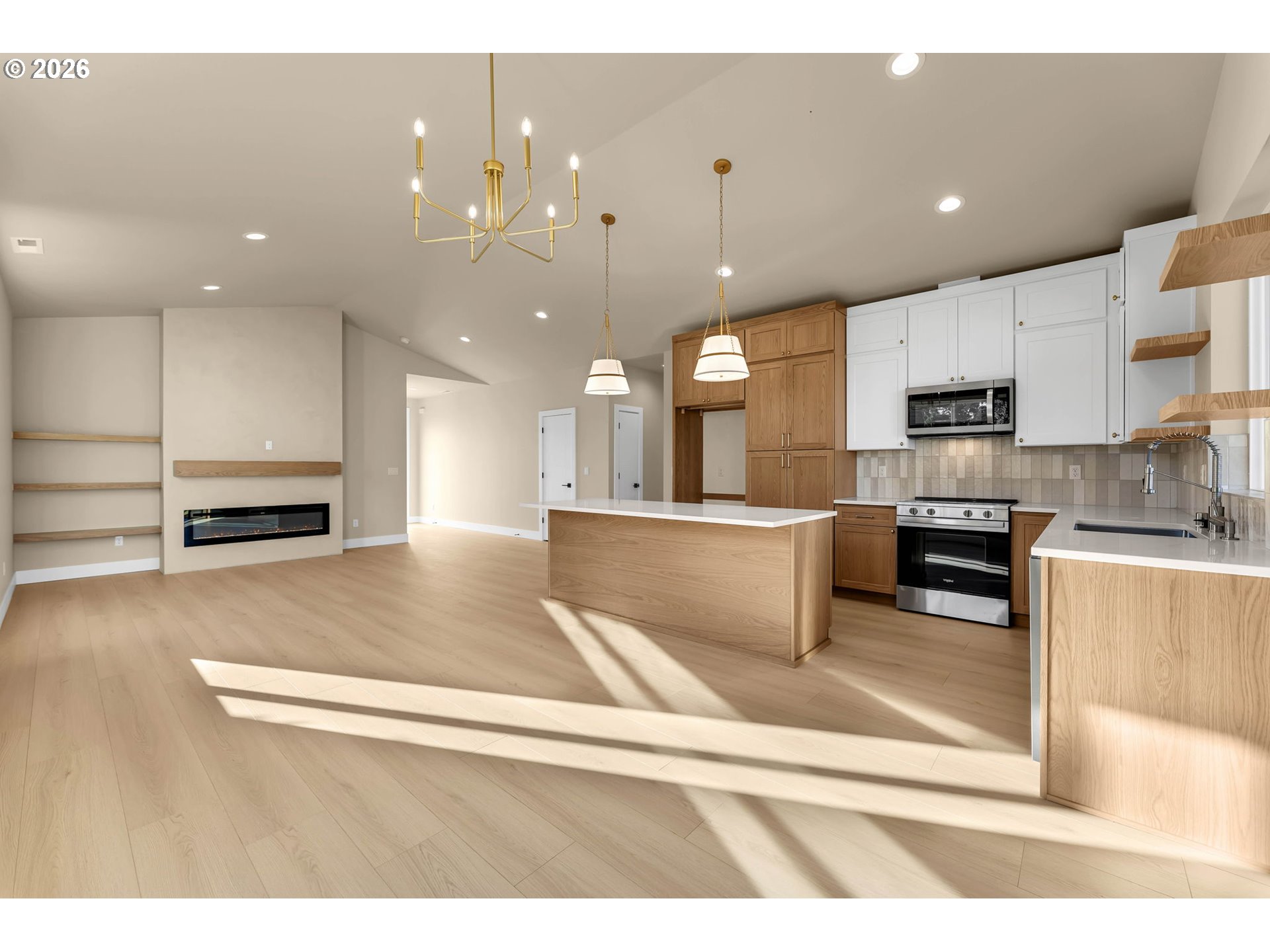 Open-plan kitchen with a large wood island, white cabinets, and a living area with a linear fireplace.