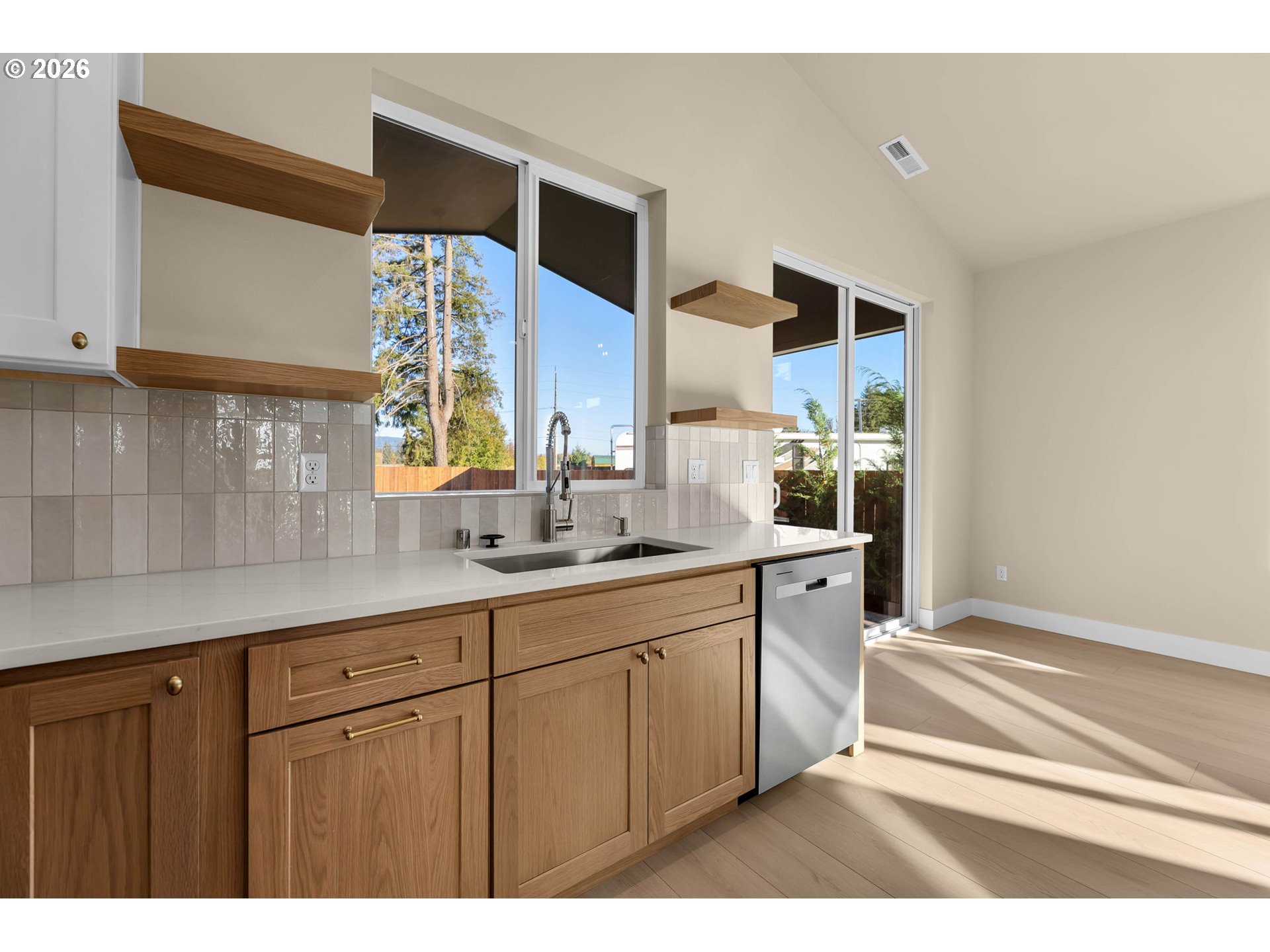 Kitchen with warm wood cabinets, white counters, and large windows beside a patio.
