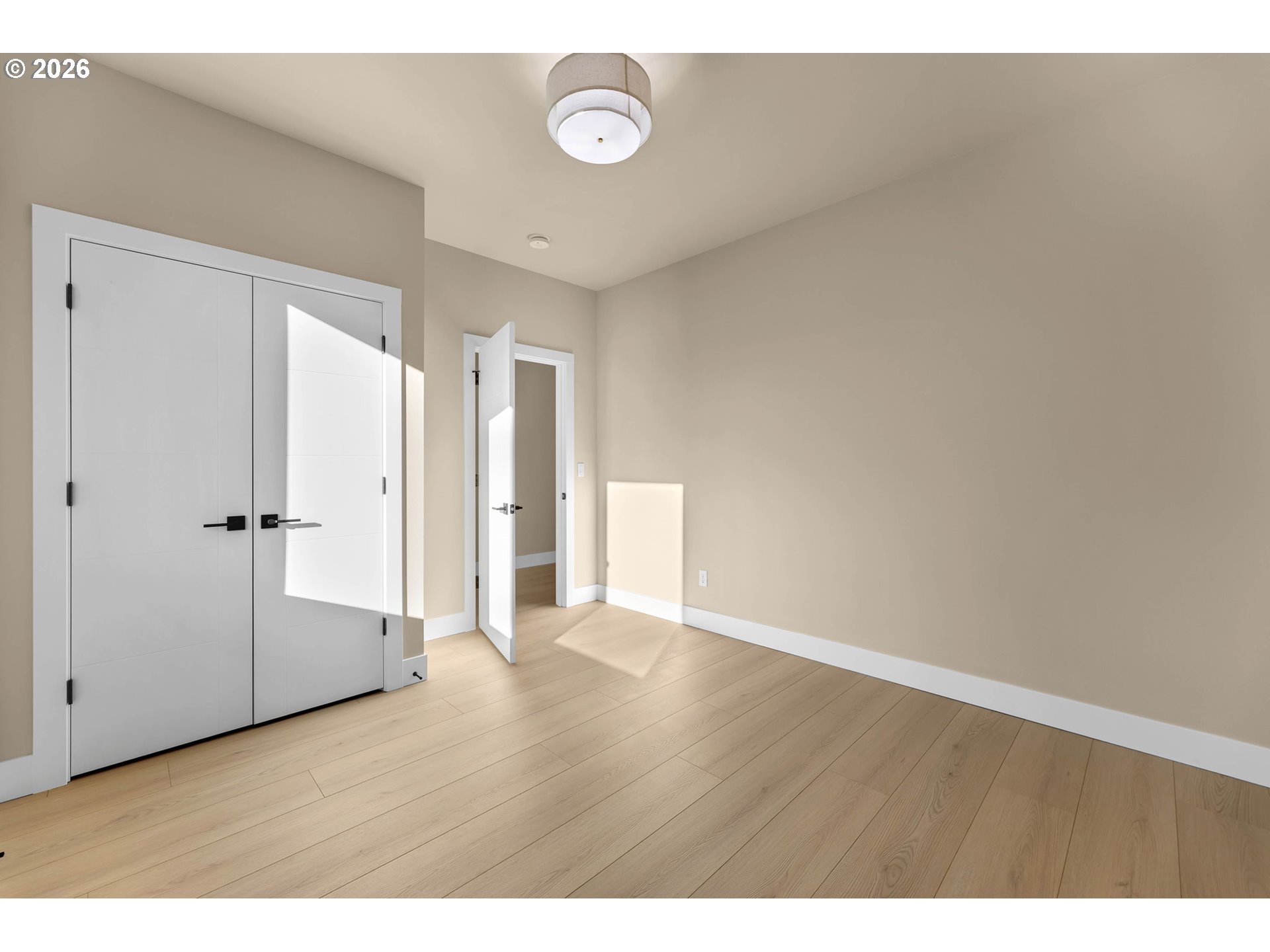 Vacant room with light wood flooring, large white closet doors, and an open doorway.
