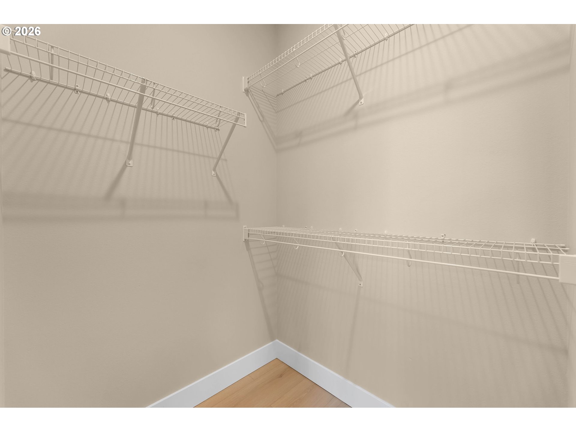 Empty walk-in closet with white wire shelving on three walls and light wood flooring.