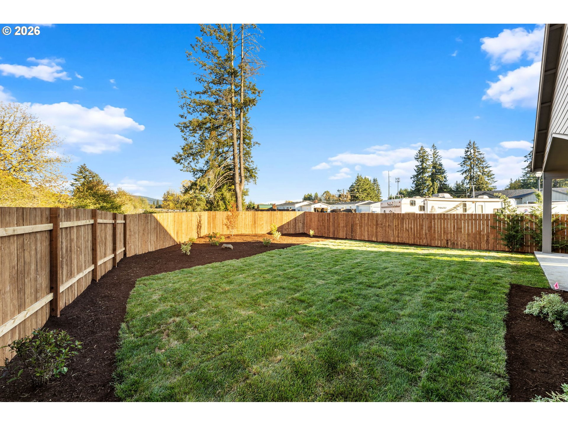 Fenced backyard with a broad lawn, curved mulch beds, and wooden privacy fencing.