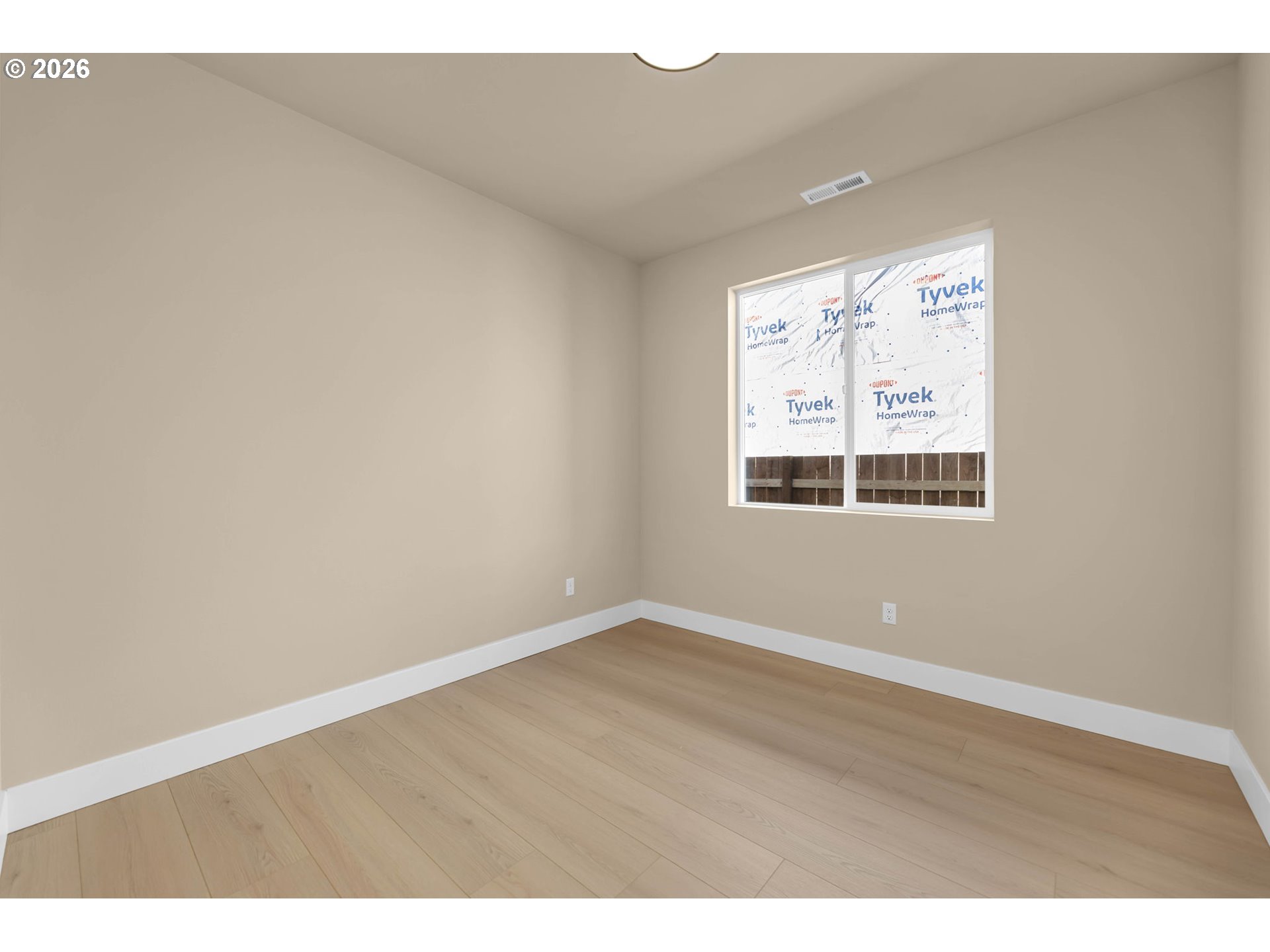 Empty room with light wood flooring and a window facing Tyvek-wrapped construction.