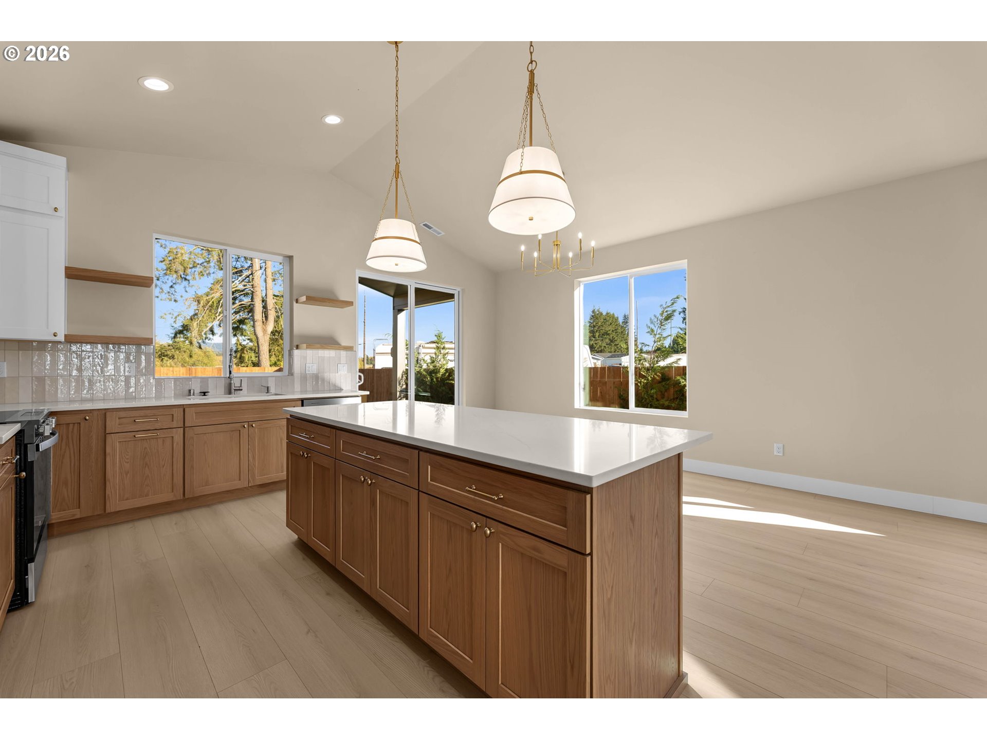 Kitchen with a large white island, warm wood cabinetry, pendant lights, and windows overlooking trees.