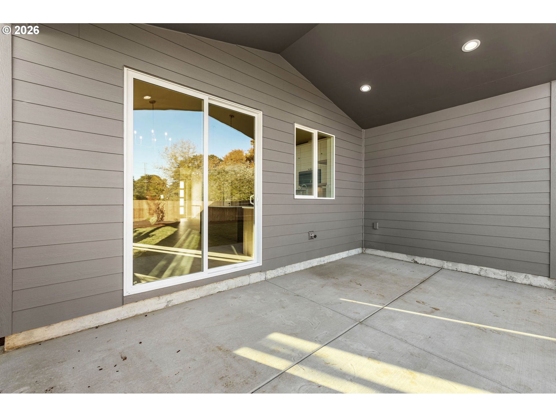 Covered concrete patio with gray siding, sliding glass doors, and recessed ceiling lights.