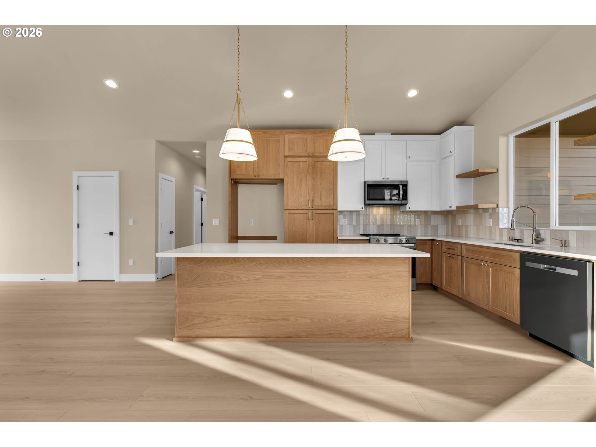 Vacant kitchen with a large wood-front island, mixed wood and white cabinets, and sunlight across the floor.