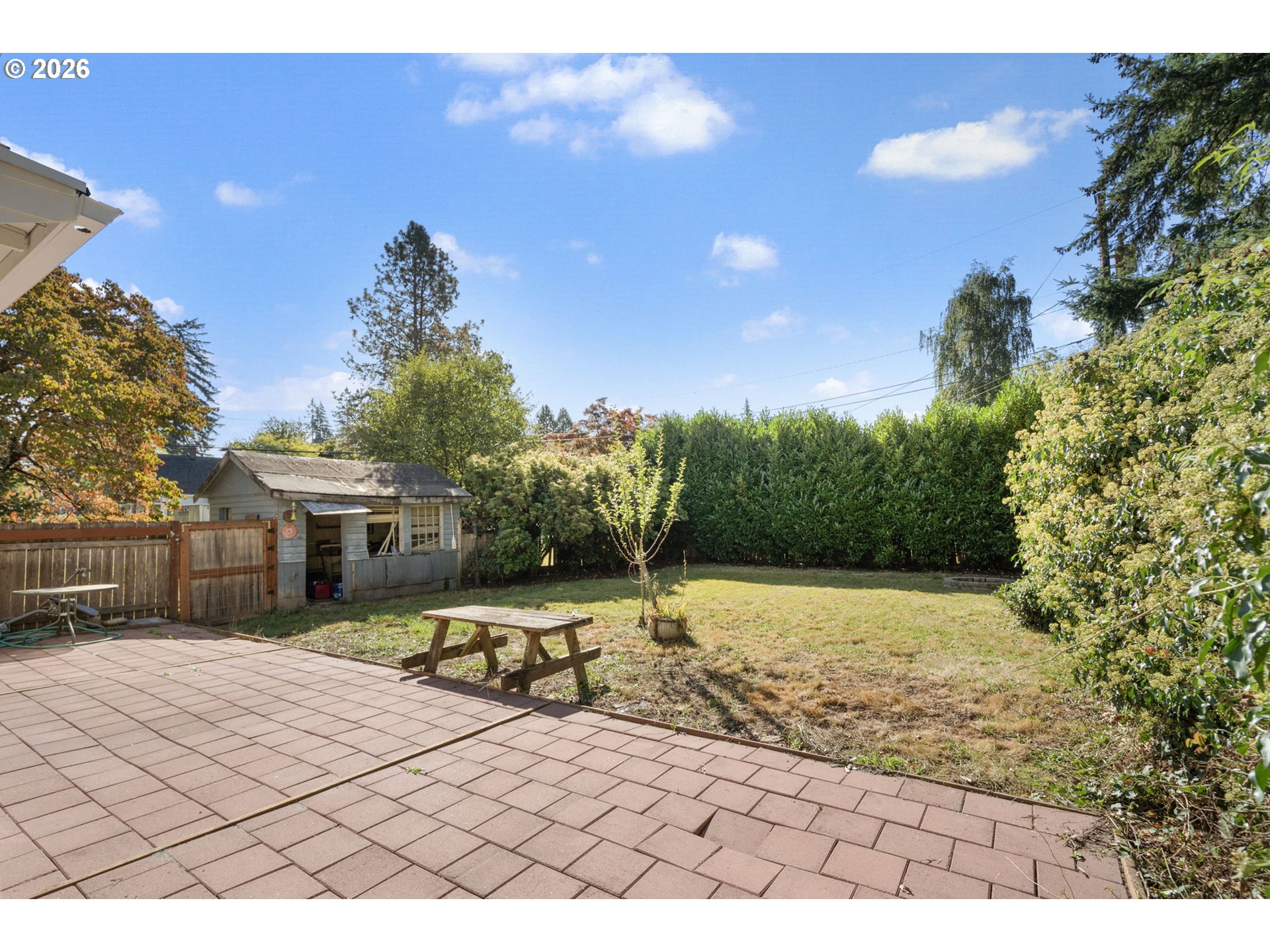 Backyard with a paved patio, picnic table, lawn, and small shed.
