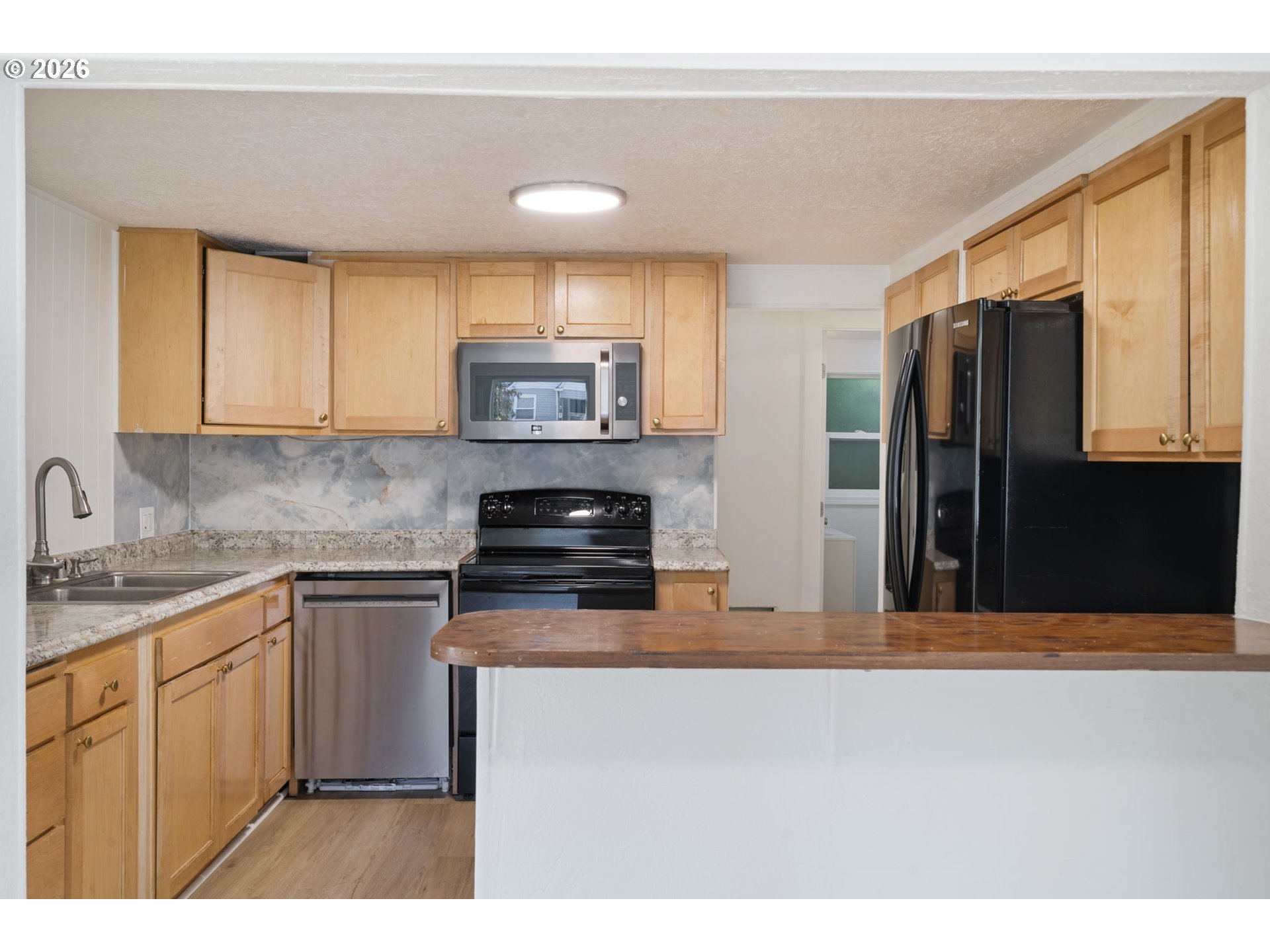 Kitchen with light wood cabinets, black appliances, and a wood-topped peninsula.
