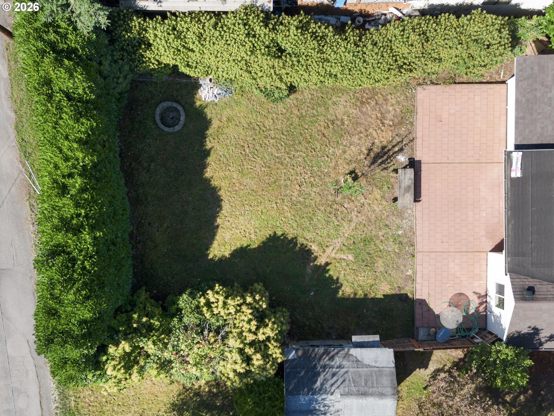 Aerial view of a hedged backyard with a circular fire pit and patio beside the house.
