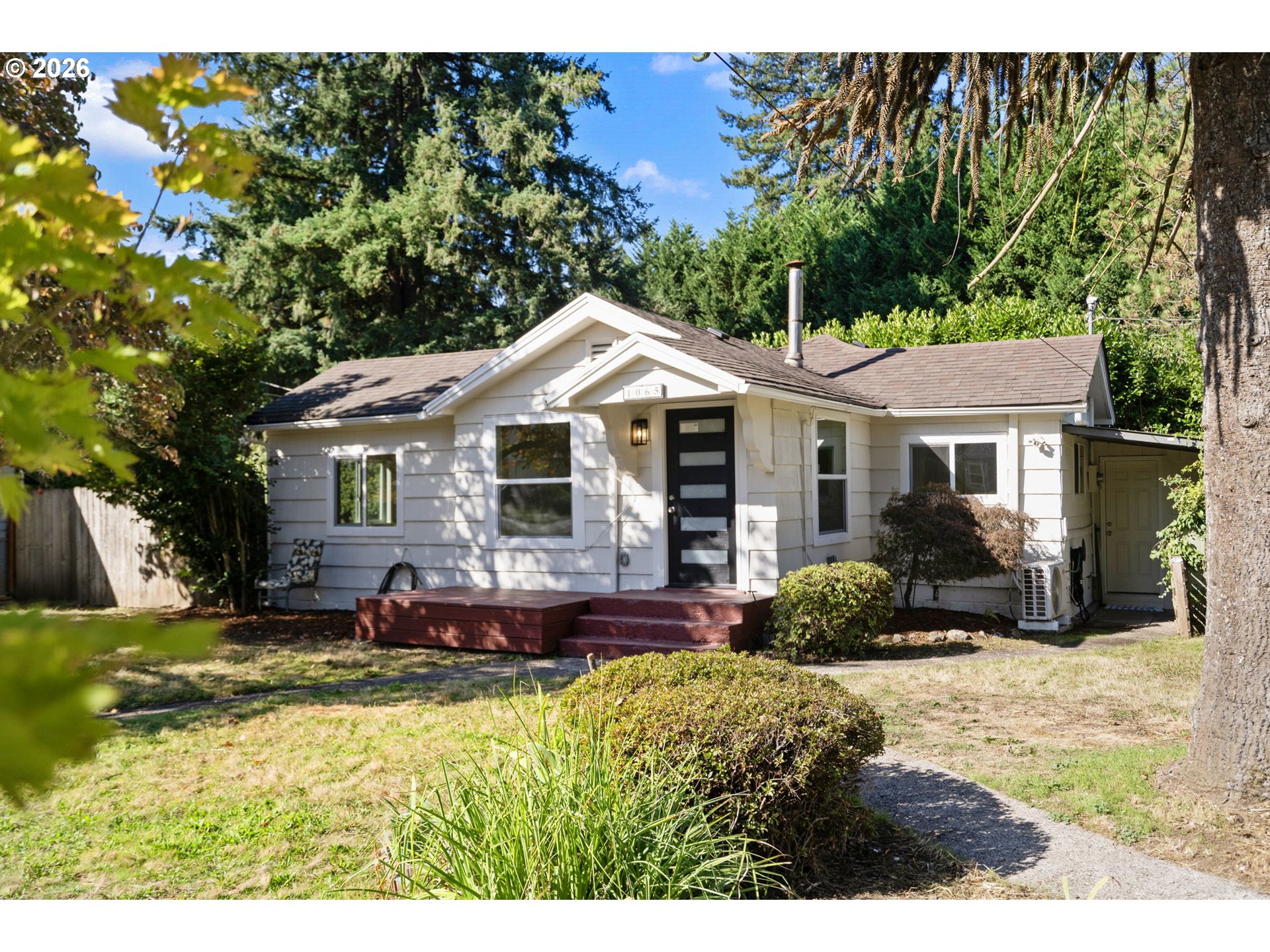 White single-story house with a dark front door, red steps, and mature trees.