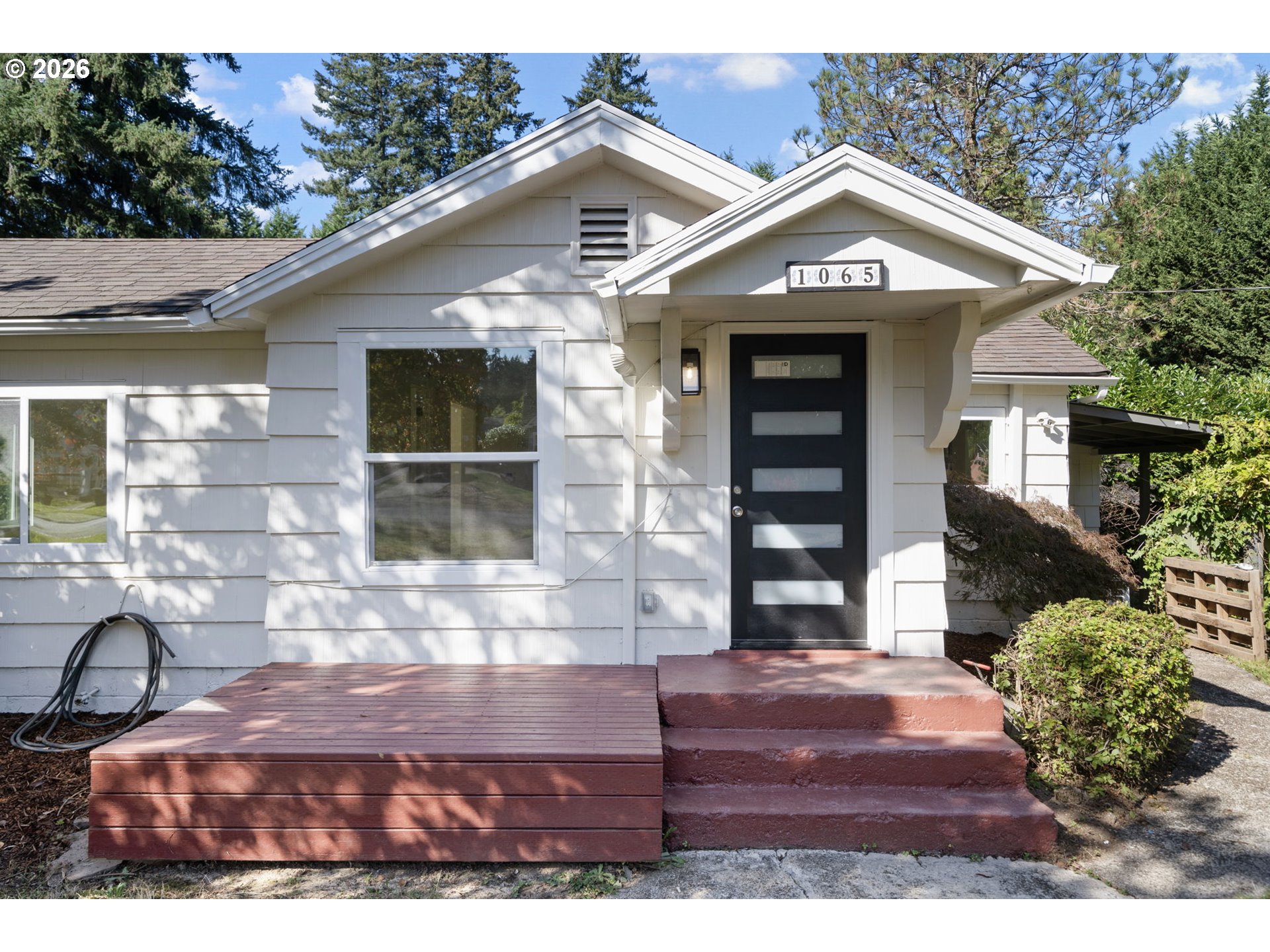 White-sided house with a black front door and red porch steps beneath the number 1065.