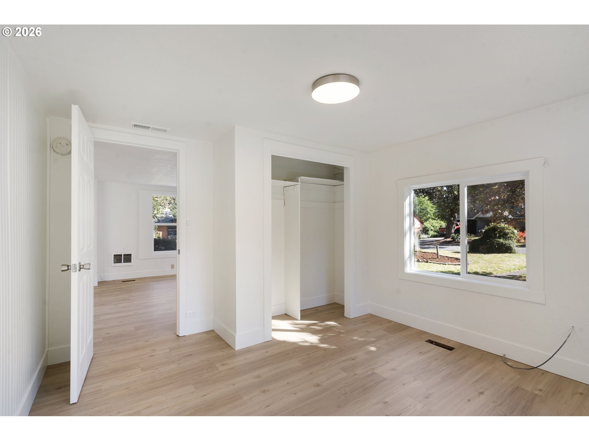 Vacant bedroom with light wood floors, an open closet, and a large window.