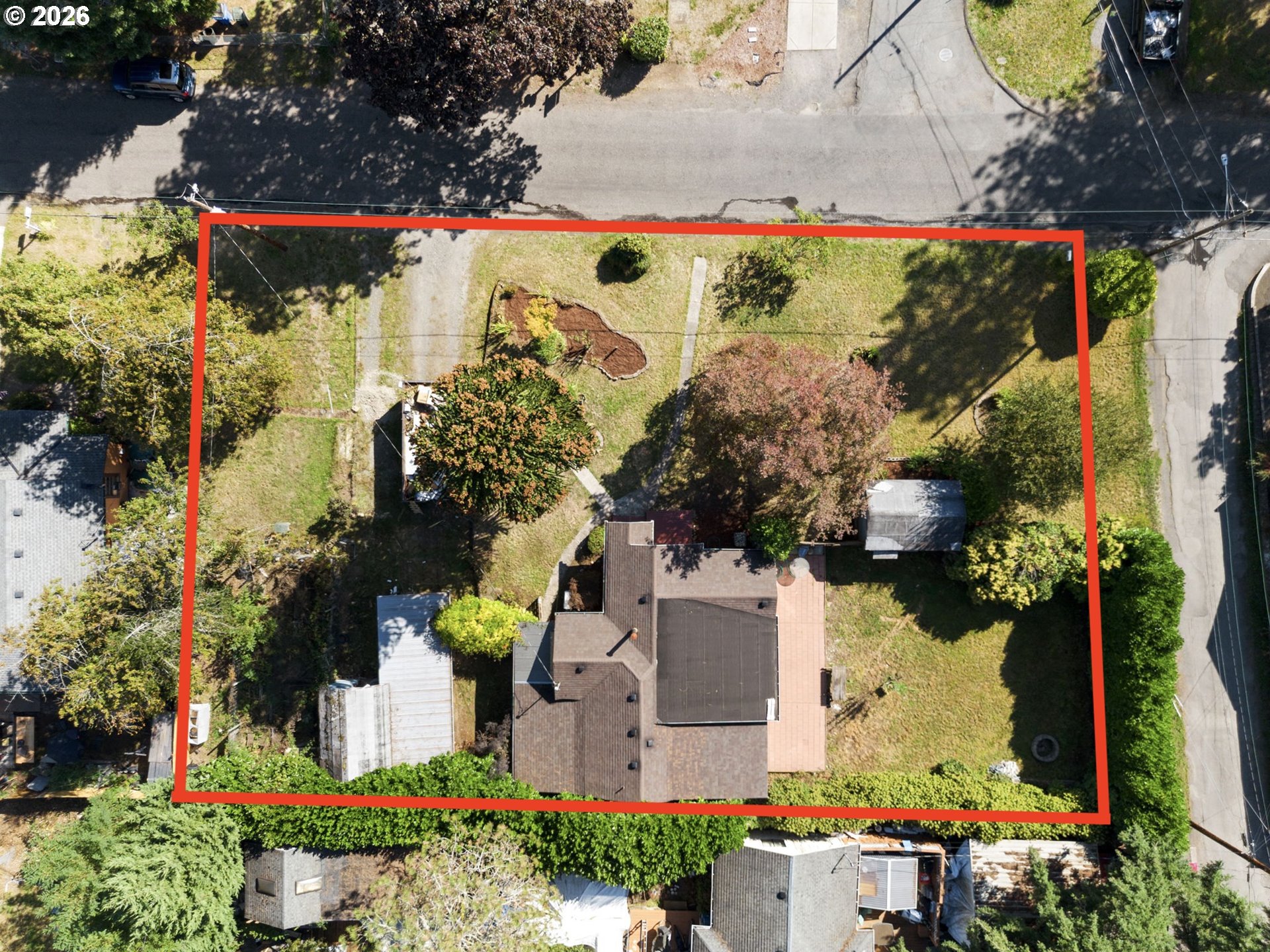 Aerial view of a house and tree-filled yard outlined in red beside the street.