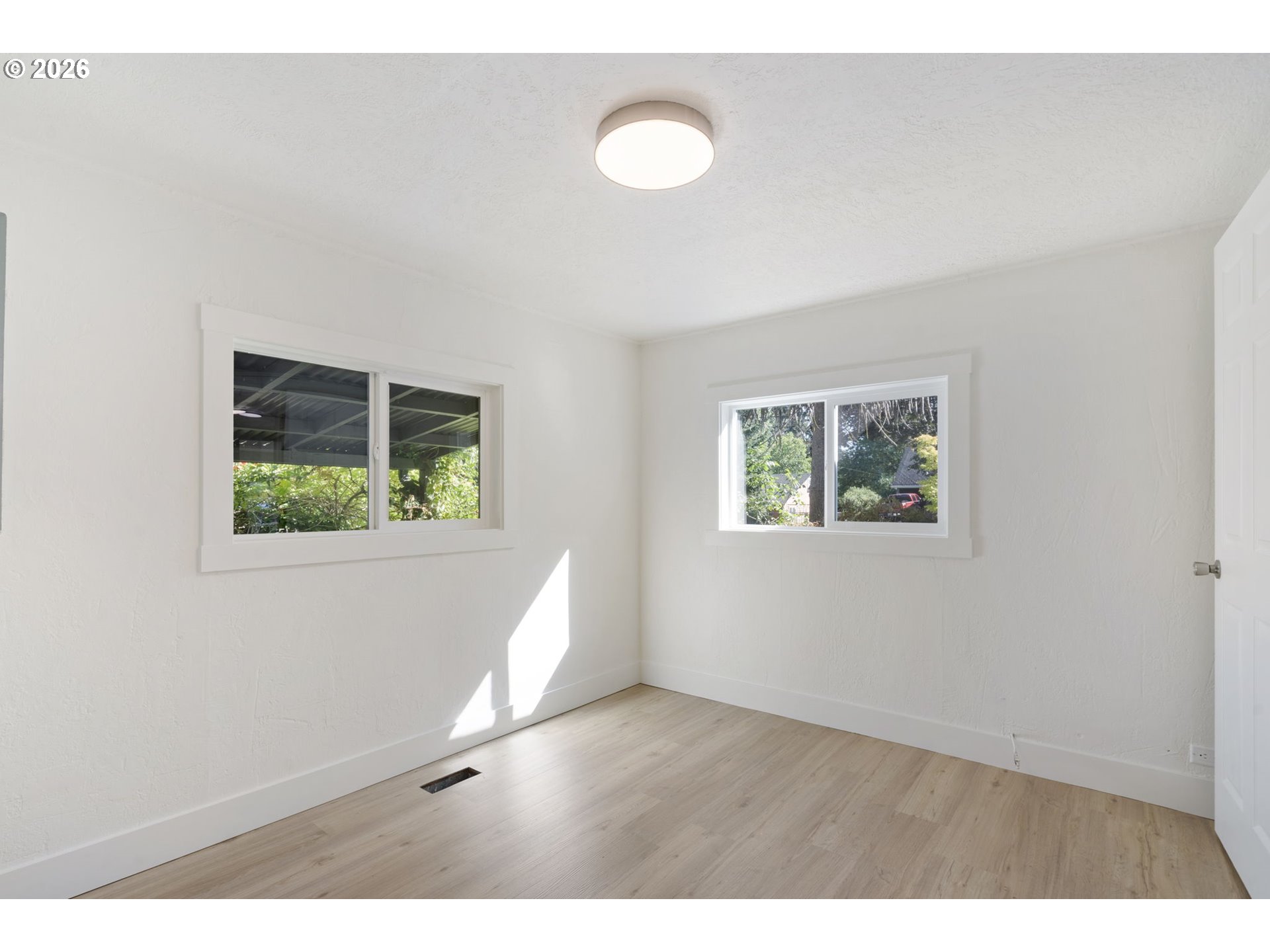 Vacant room with light wood flooring, two windows, and sunlight across the floor.