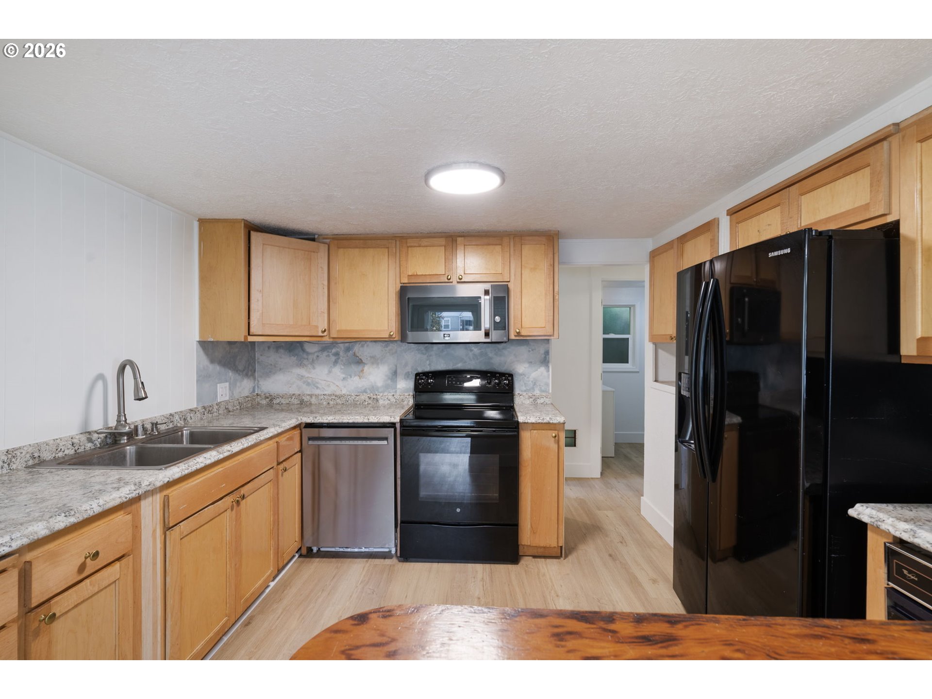 Kitchen with light wood cabinets, speckled countertops, and black refrigerator and range.