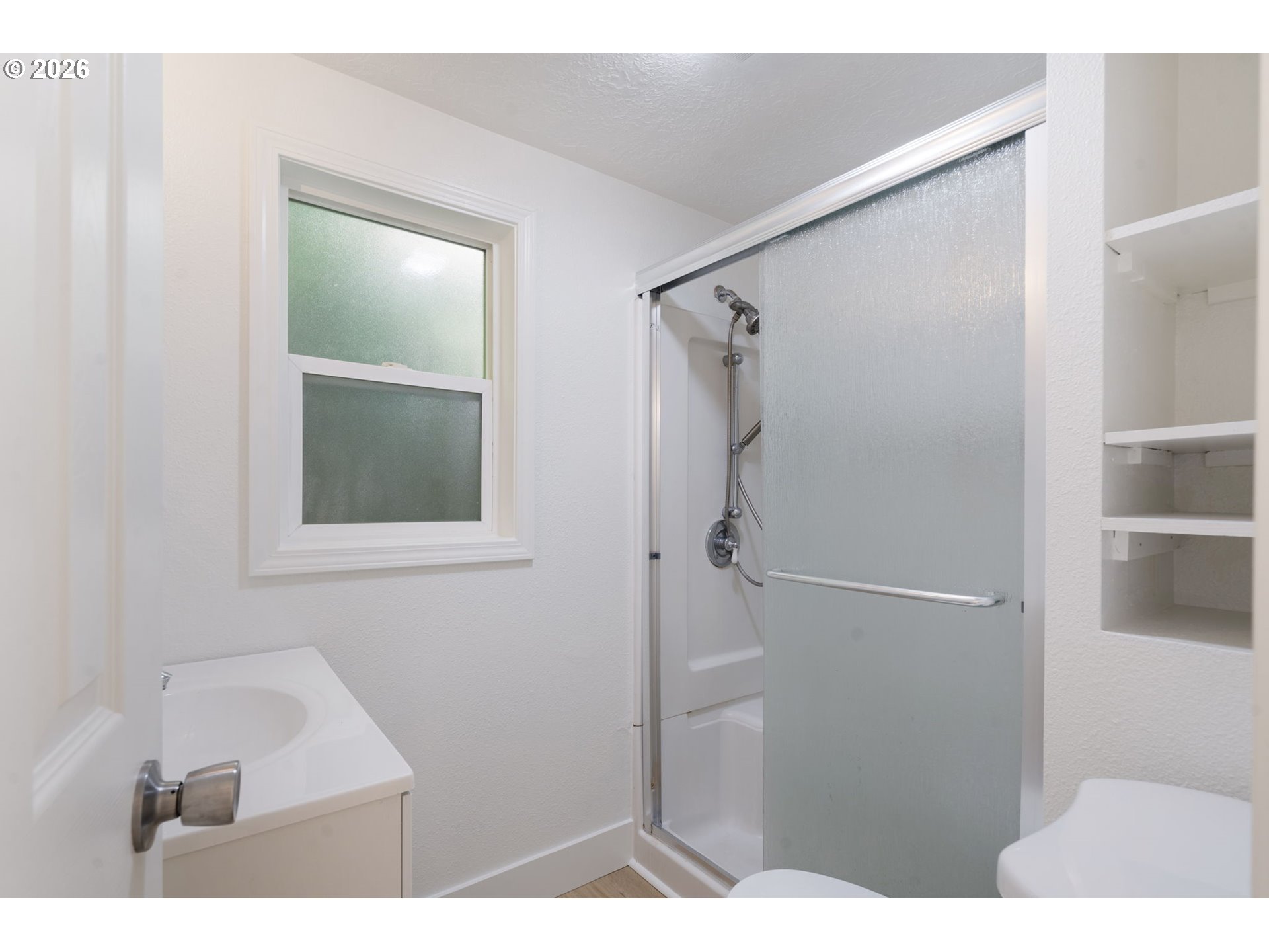 Bathroom with a frosted window, glass shower door, and built-in shelves.